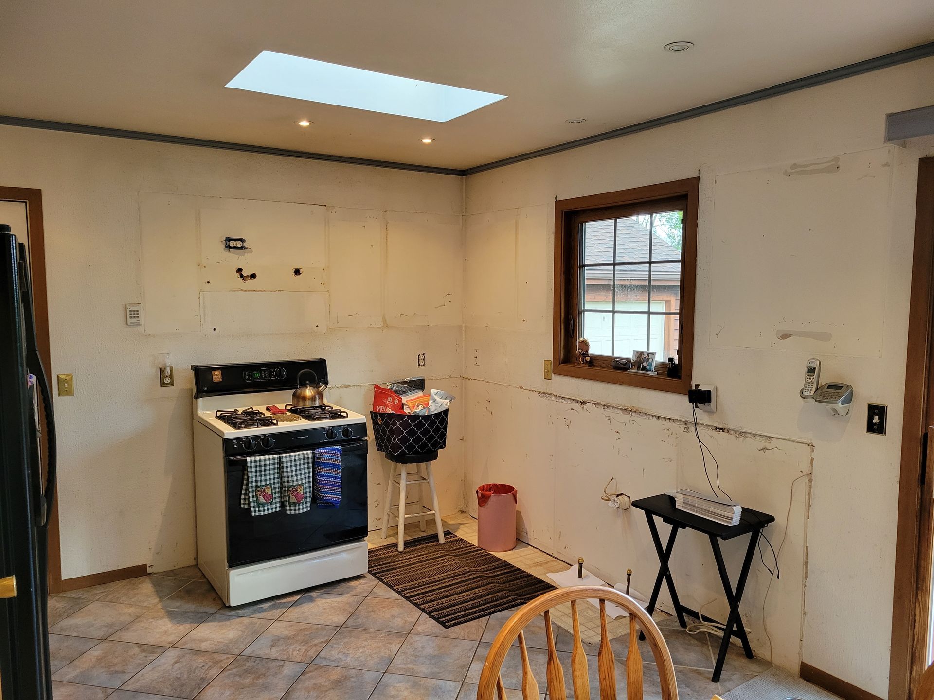 Small unfinished kitchen with a stove, window, skylight, and folding table in a bare room