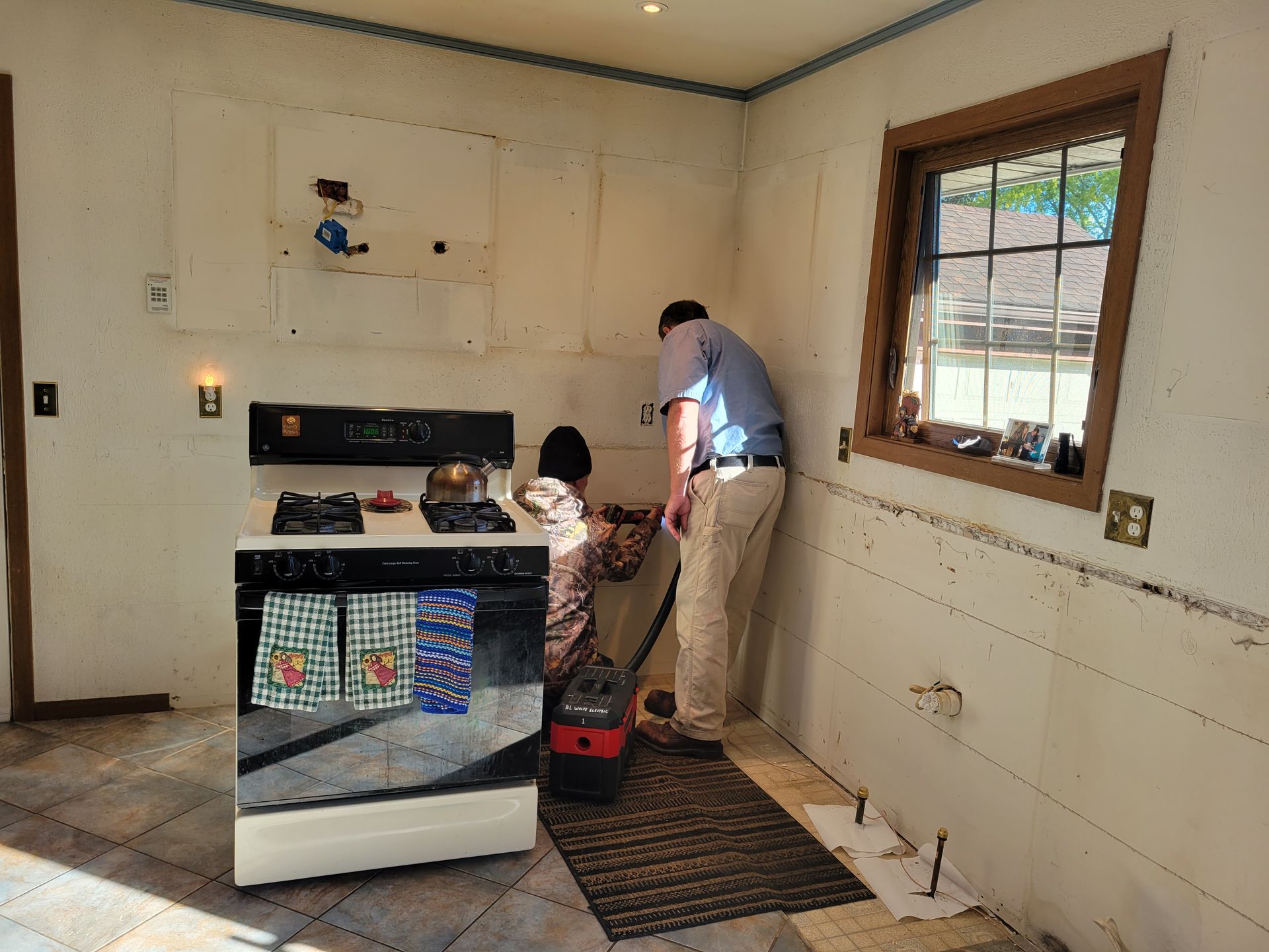 Person cleaning kitchen floor beside stove in a small room with a window and tile floor