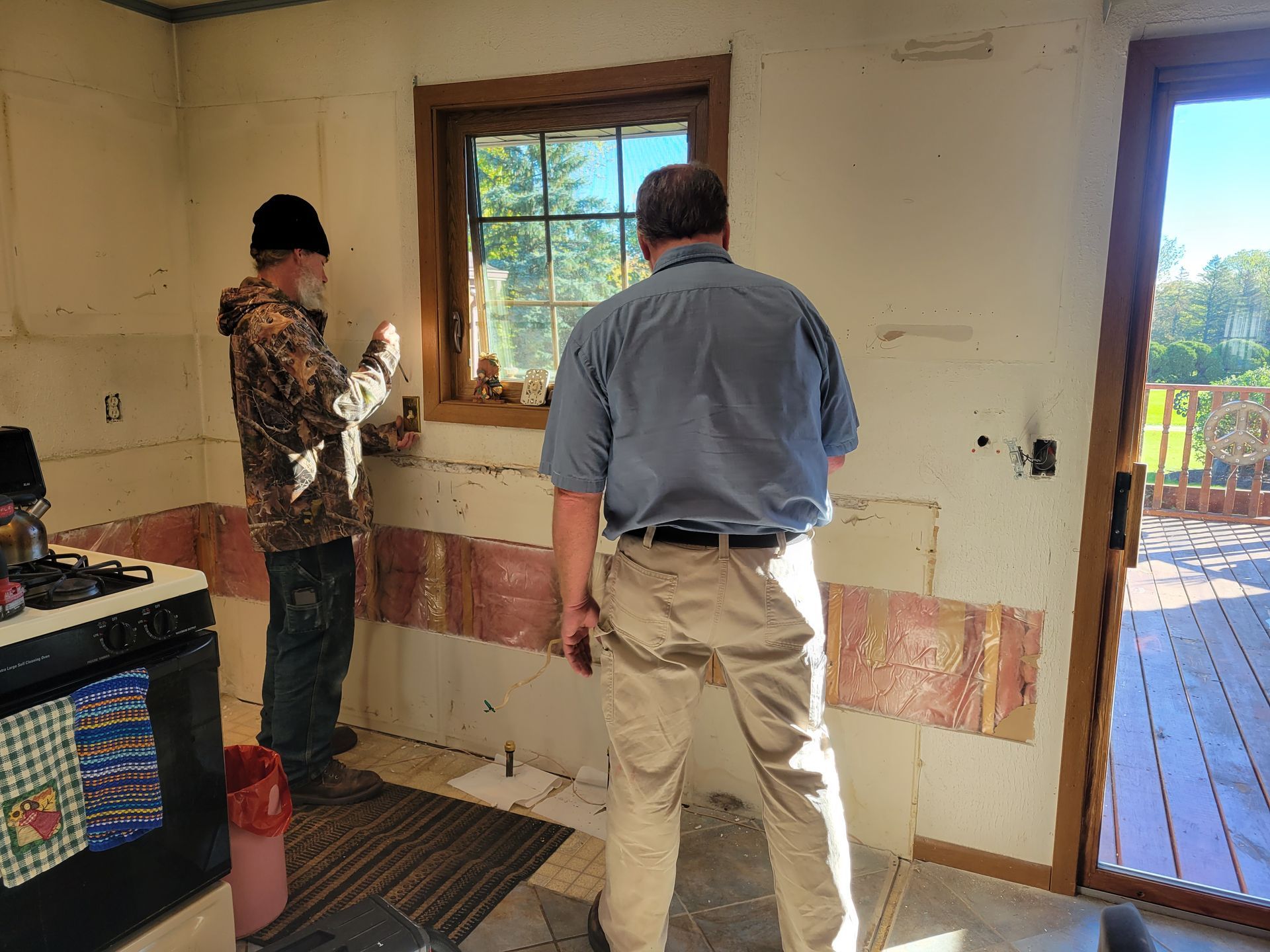 Two people standing in a room under renovation, facing a window and wall, with tools nearby.
