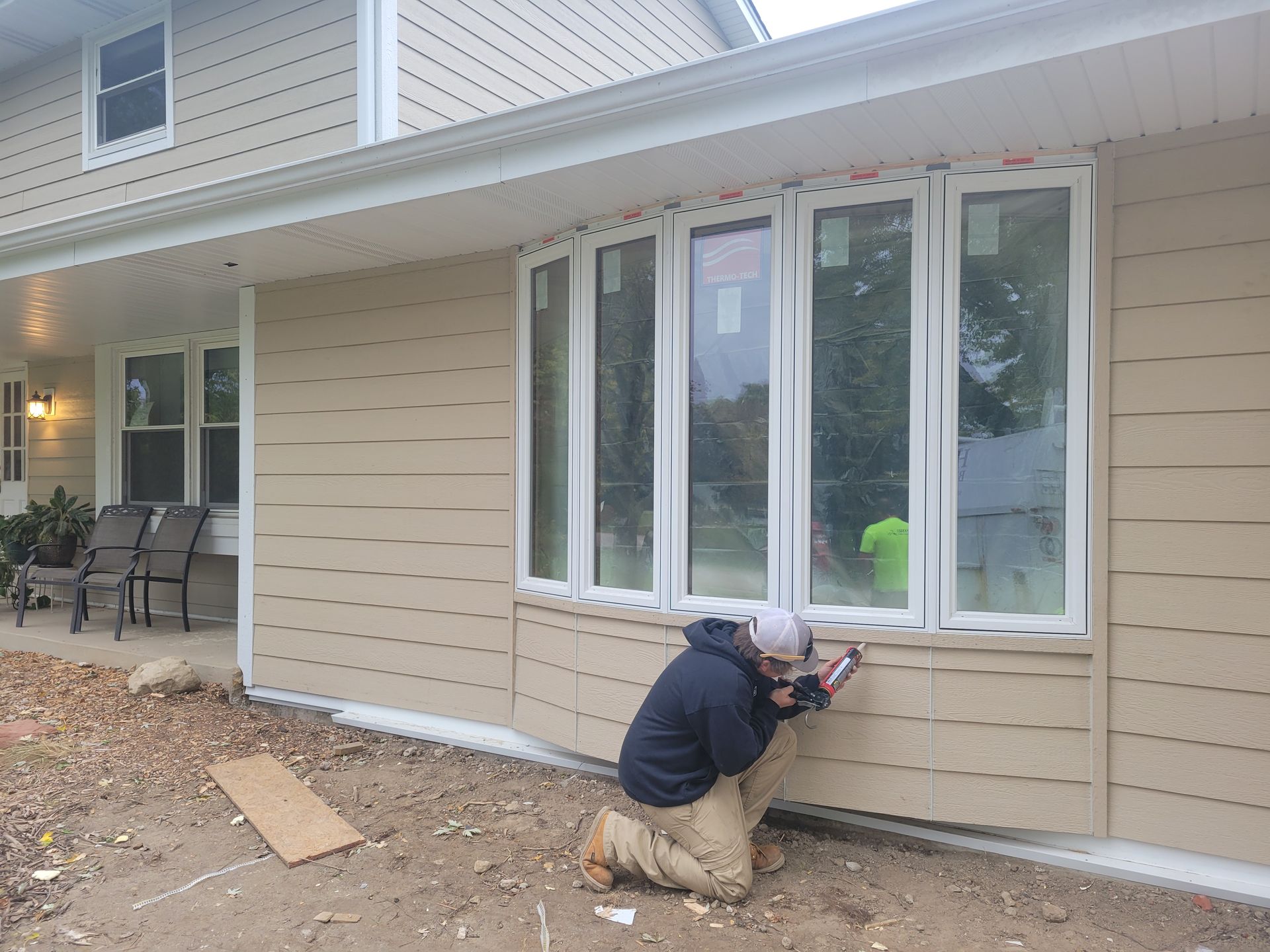 Worker caulking around a white-trimmed window on a beige house exterior