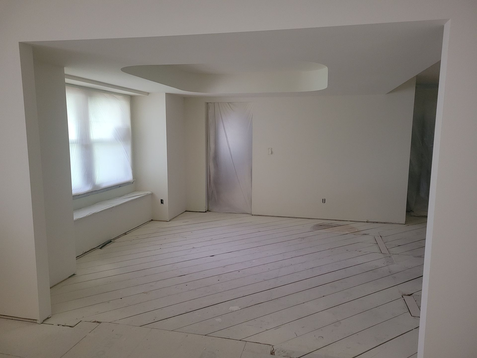 Empty white room with large windows and light-colored flooring under renovation