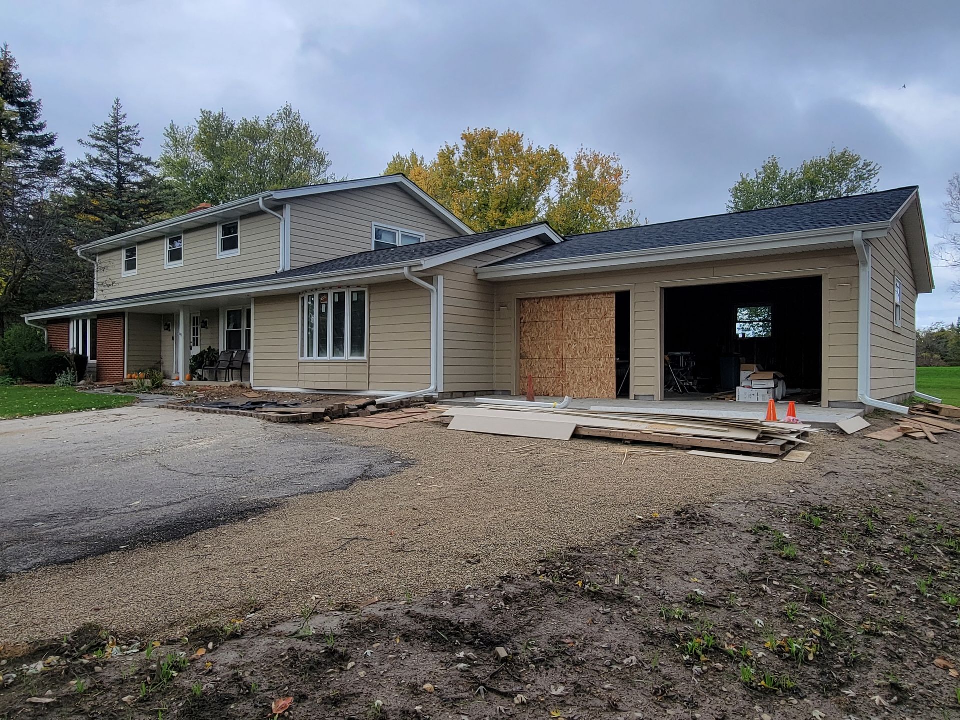 Suburban house under construction with unfinished garage, gravel driveway, and bare dirt front yard