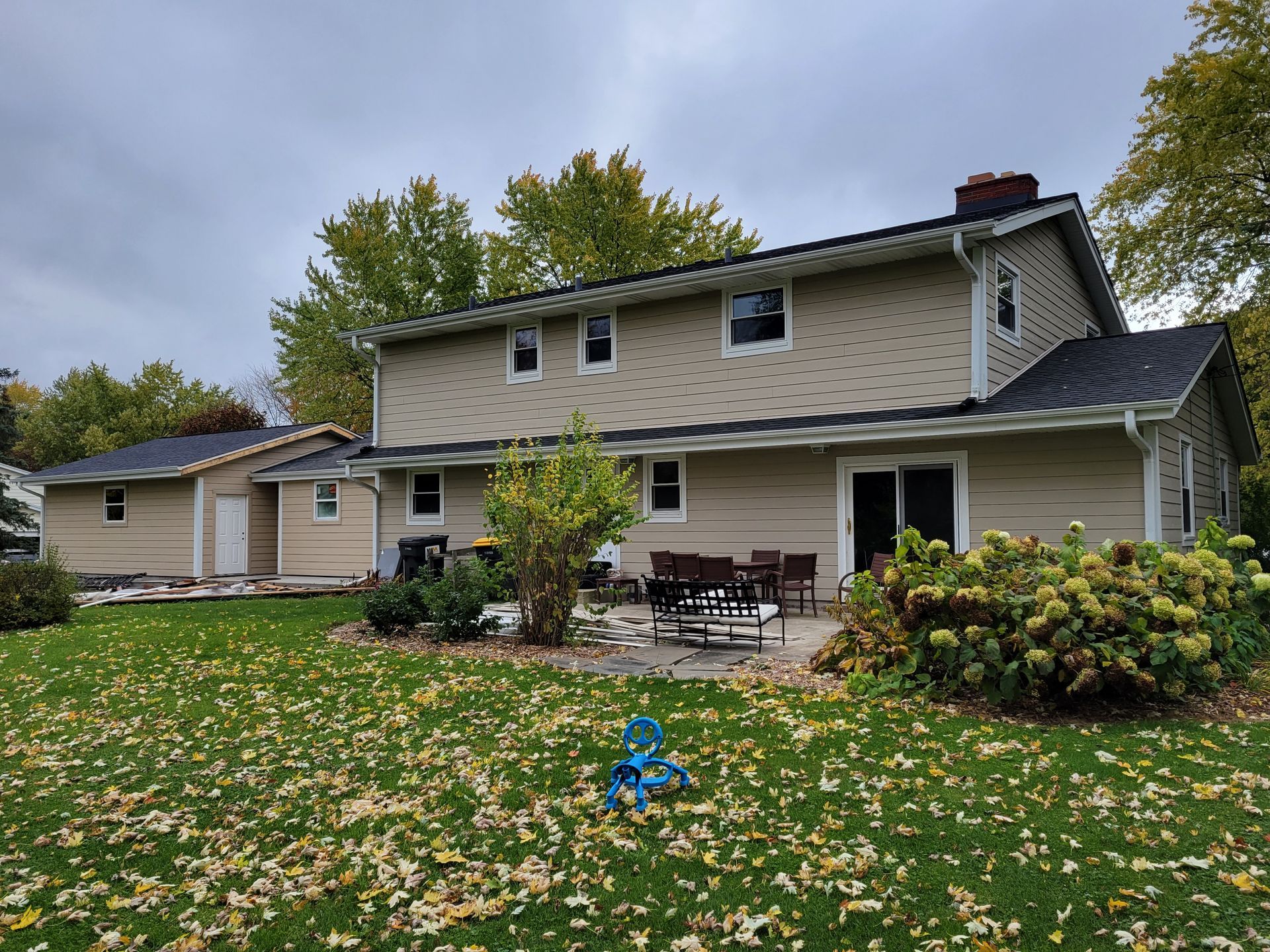 Two-story beige house with a front porch and autumn leaves on the lawn