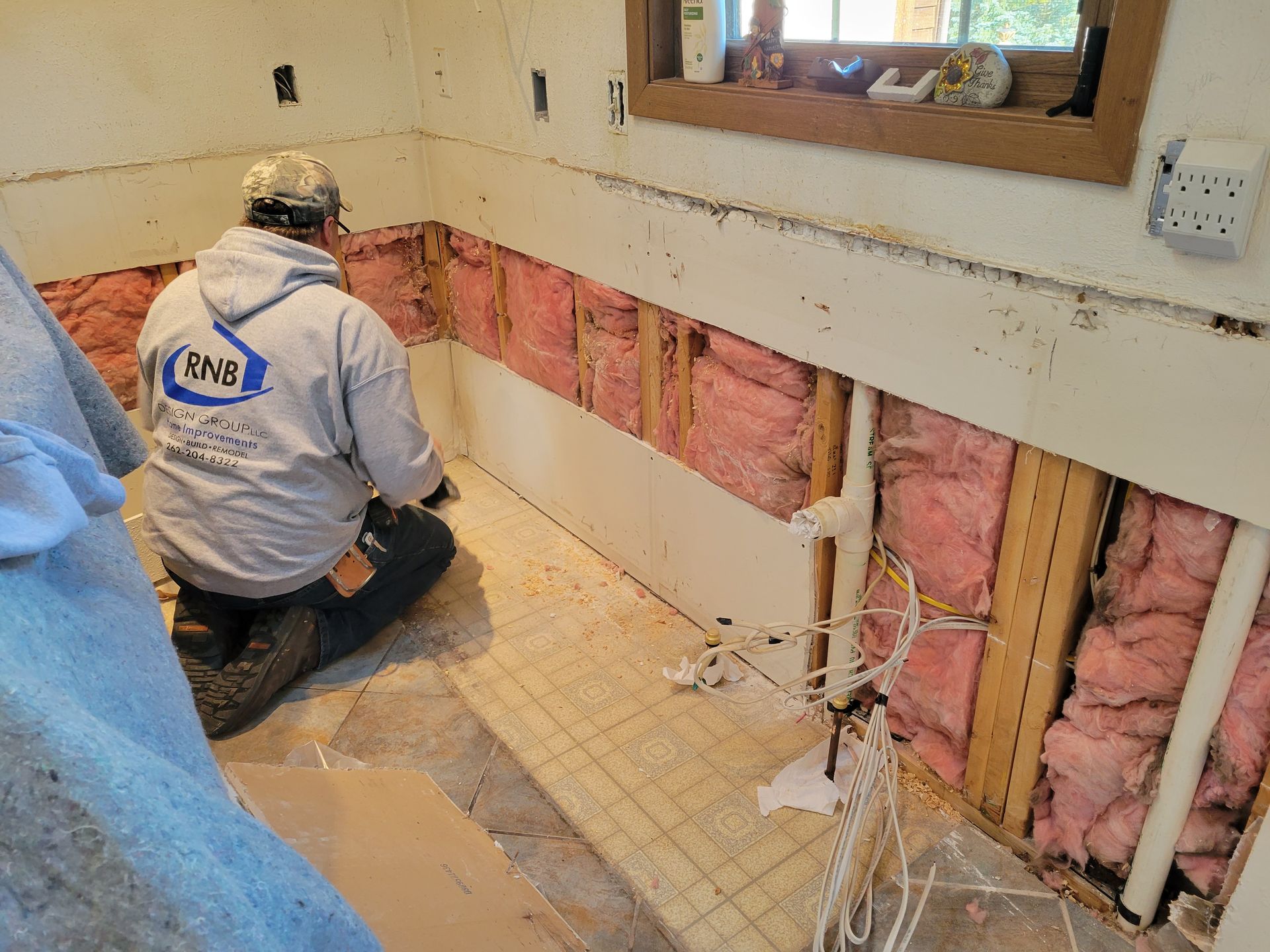 Worker installing pink insulation in a wall during home renovation