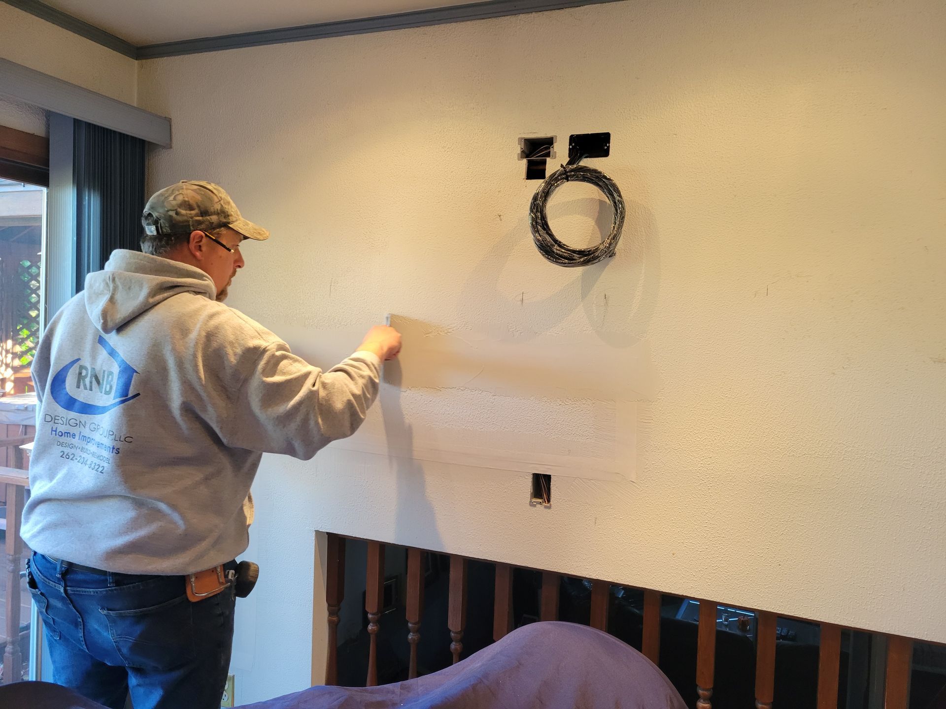 Worker installing wall-mounted fixture in a room with beige walls and a small window.