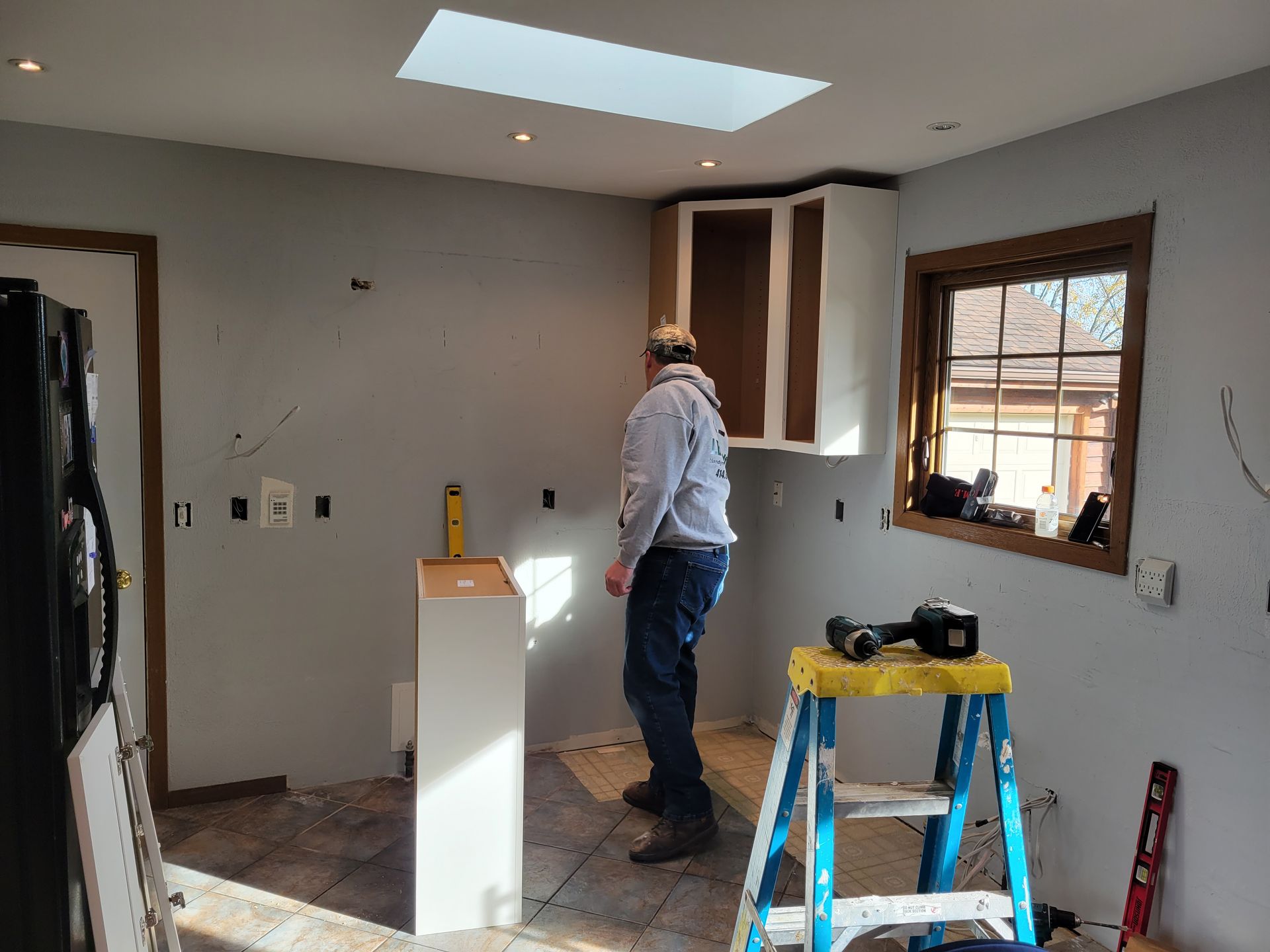 Person working on kitchen renovation with ladders, tools, and unfinished cabinets