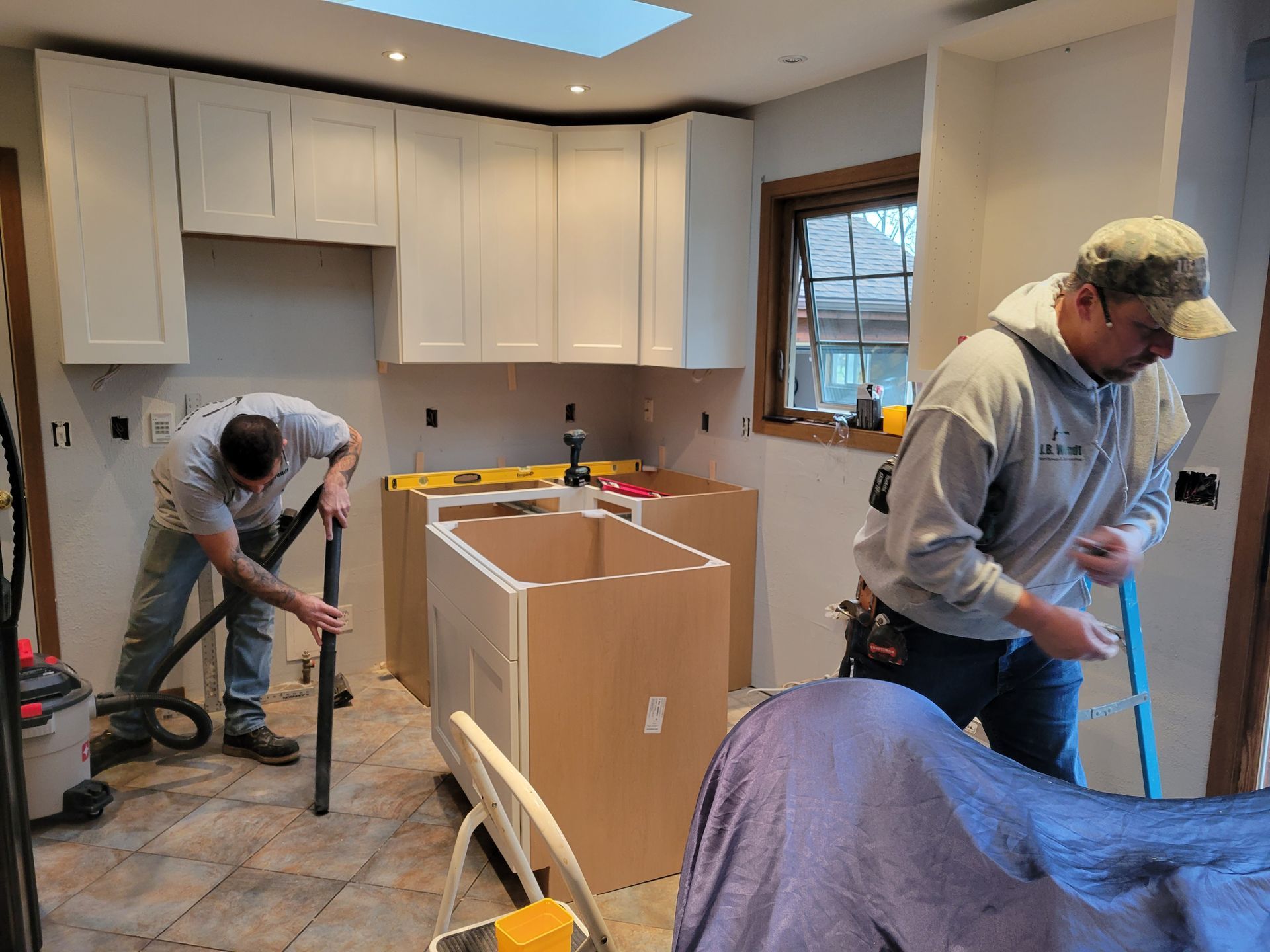 People cleaning a kitchen under renovation, with boxes and tools on the floor.