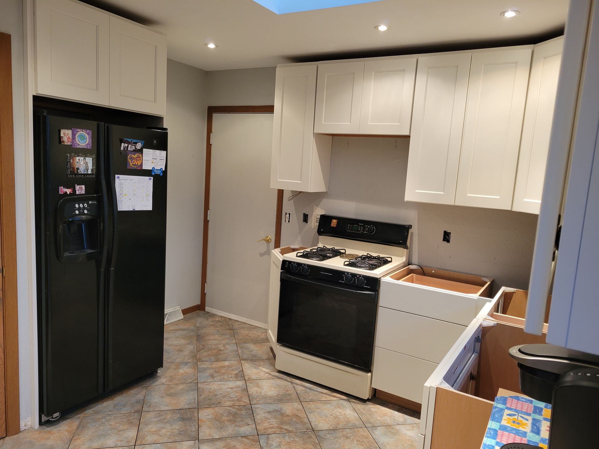 Small kitchen with black refrigerator, white cabinets, stove, and tiled floor.