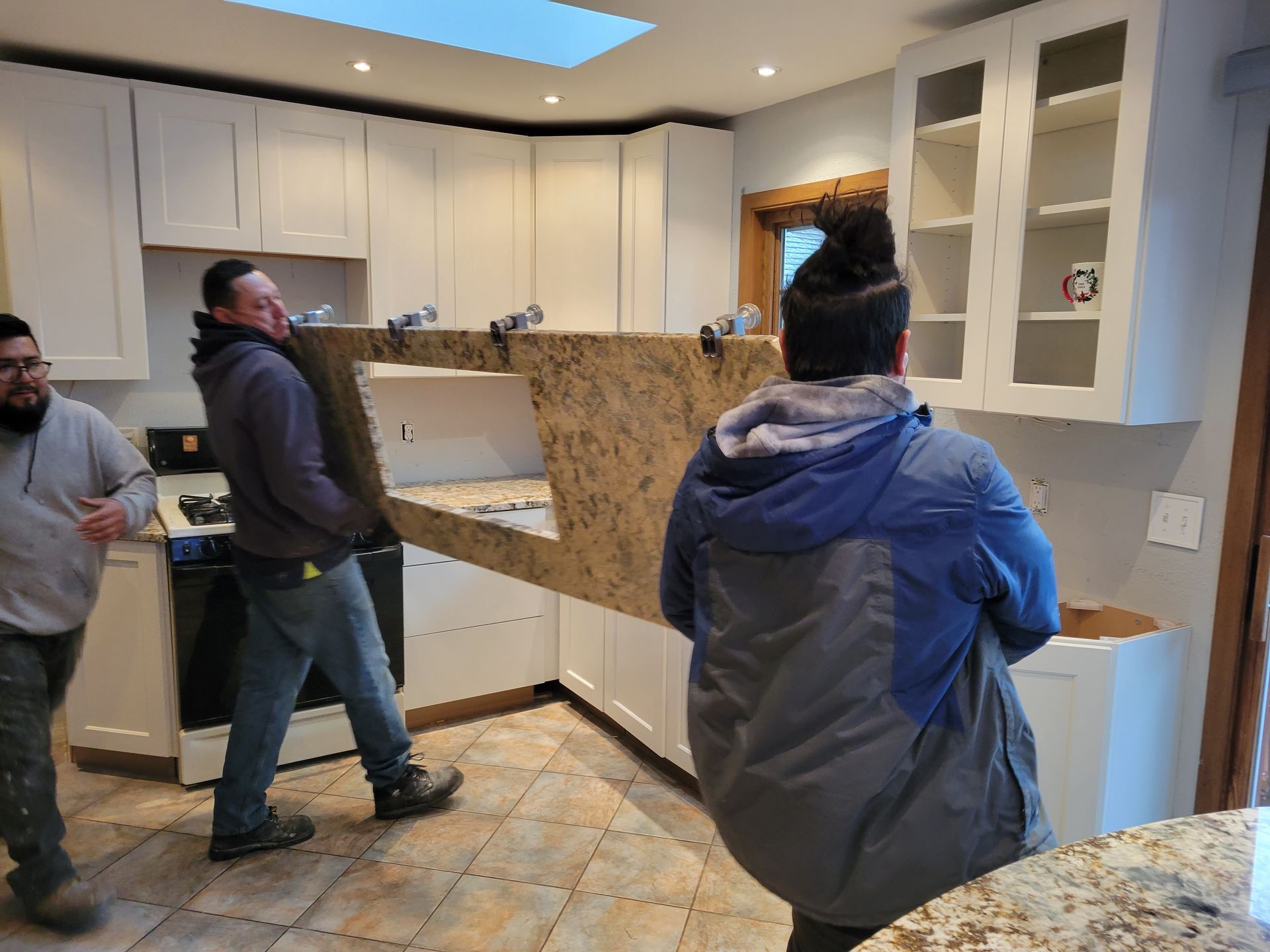 Workers moving a large granite countertop through a bright kitchen under renovation