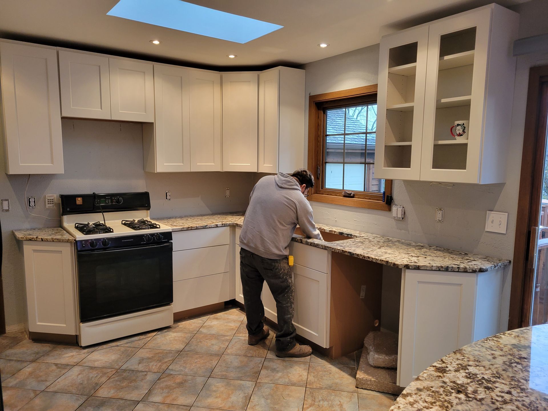 Person renovating a kitchen with white cabinets, granite counters, and a black stove.