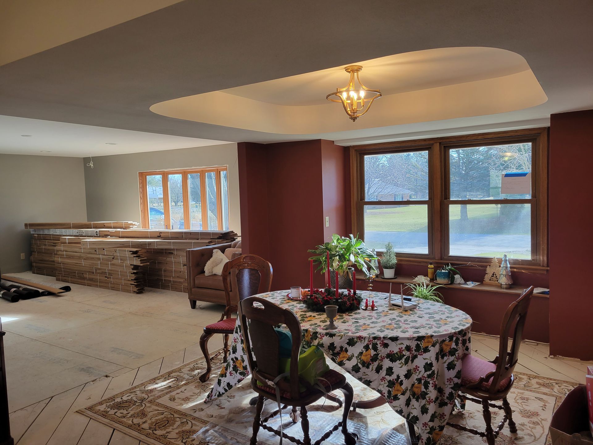 Dining room with round floral tablecloth, wooden chairs, large windows, and stone fireplace under a tray ceiling