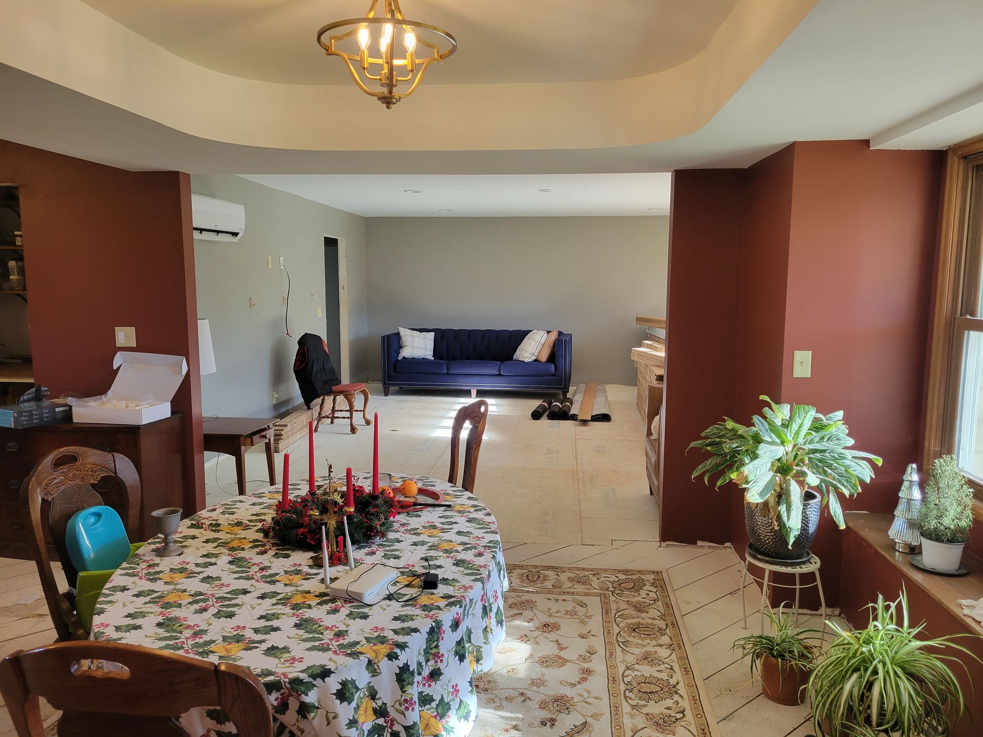Dining room with floral tablecloth, plants, and a sofa in a sunken living area beyond.