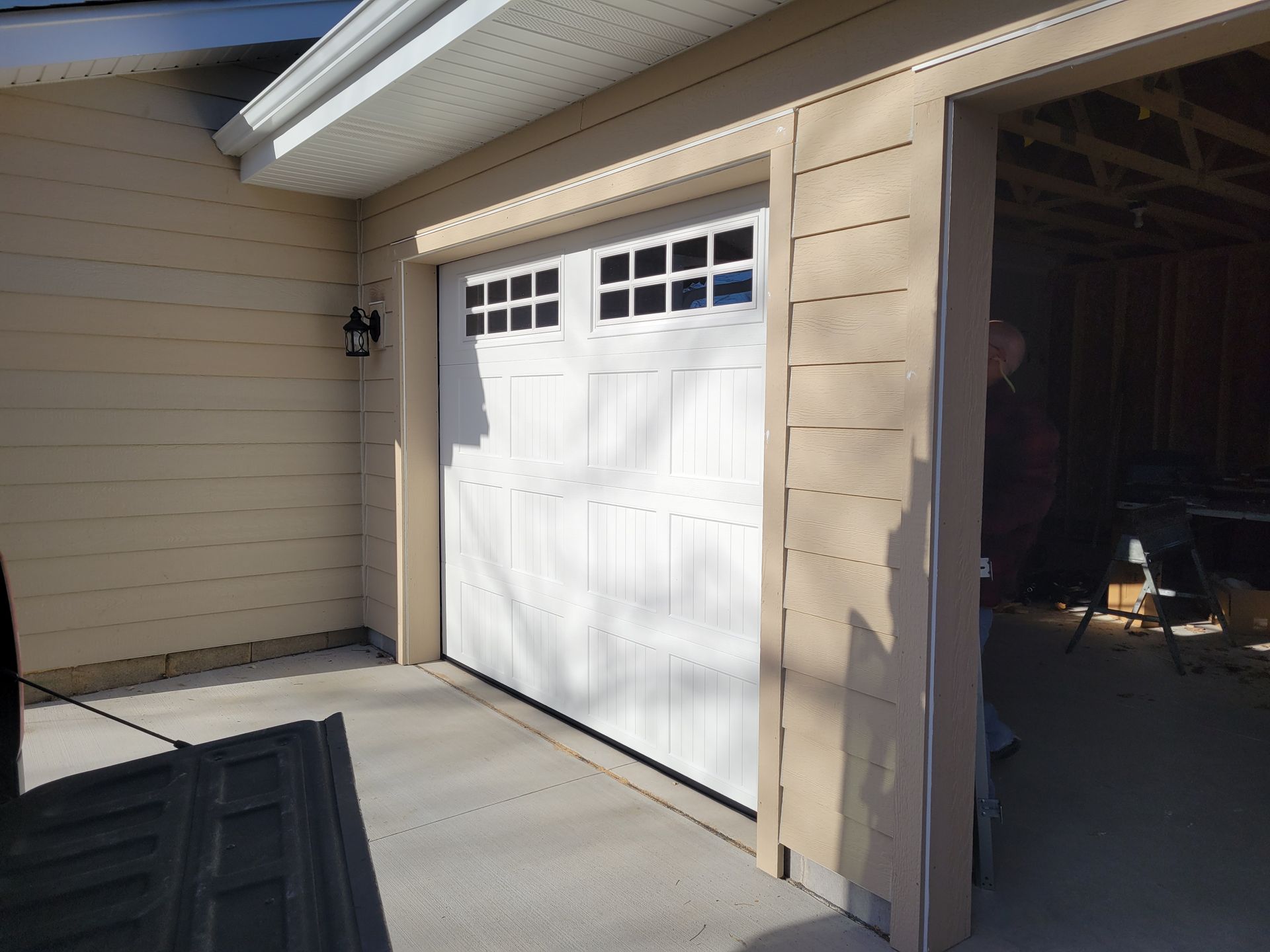 Residential garage with white door, beige siding, and an open side entrance showing the interior.