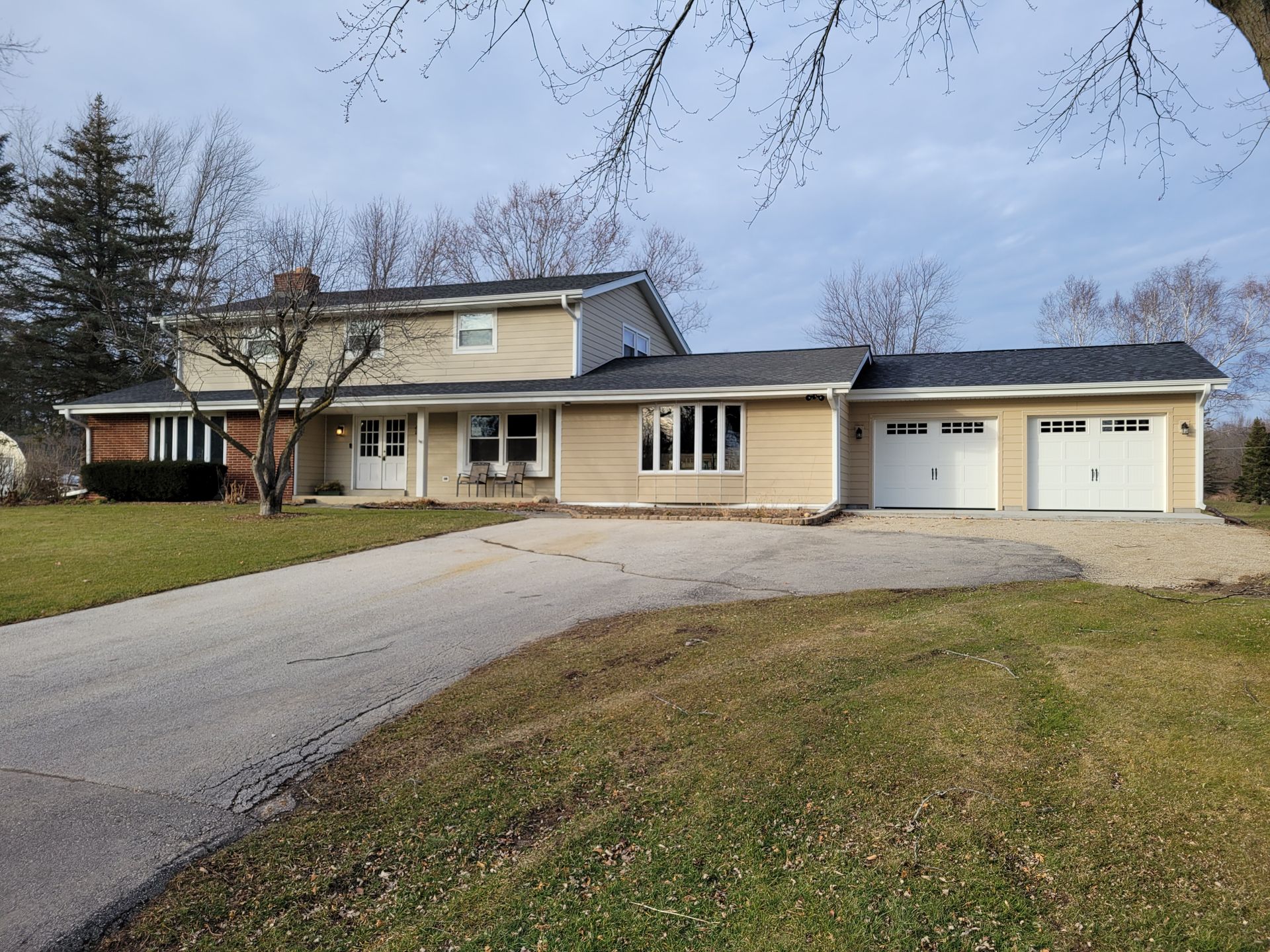 Suburban two-story house with beige siding, two garages, and a curved driveway on a cloudy day