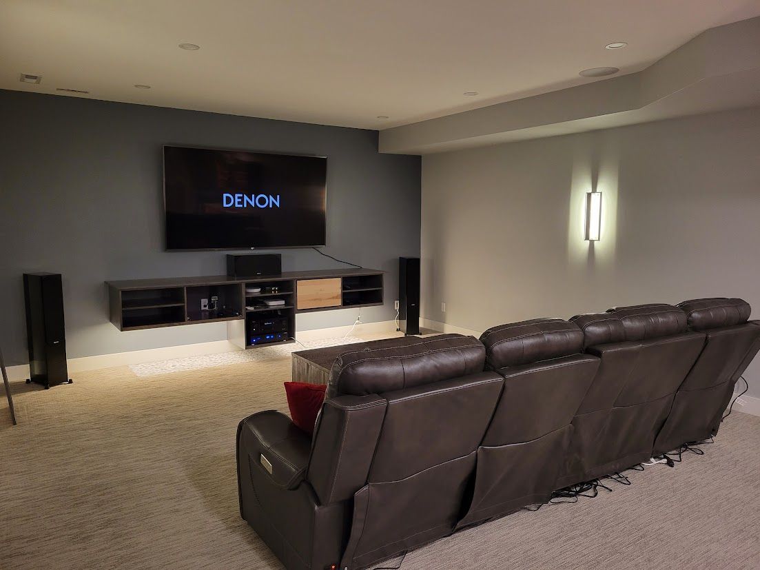 Modern media room with a wall-mounted TV, soundbar, and black leather recliner sofa.