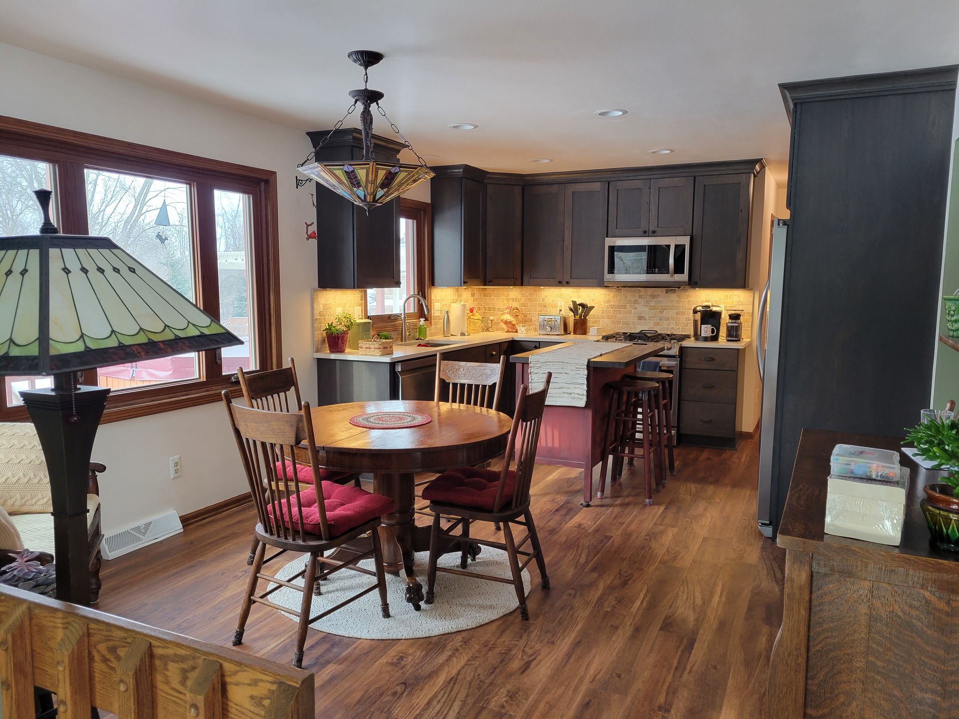Open-plan kitchen and dining area with wood floors, round table, dark cabinets, and stained-glass lamp