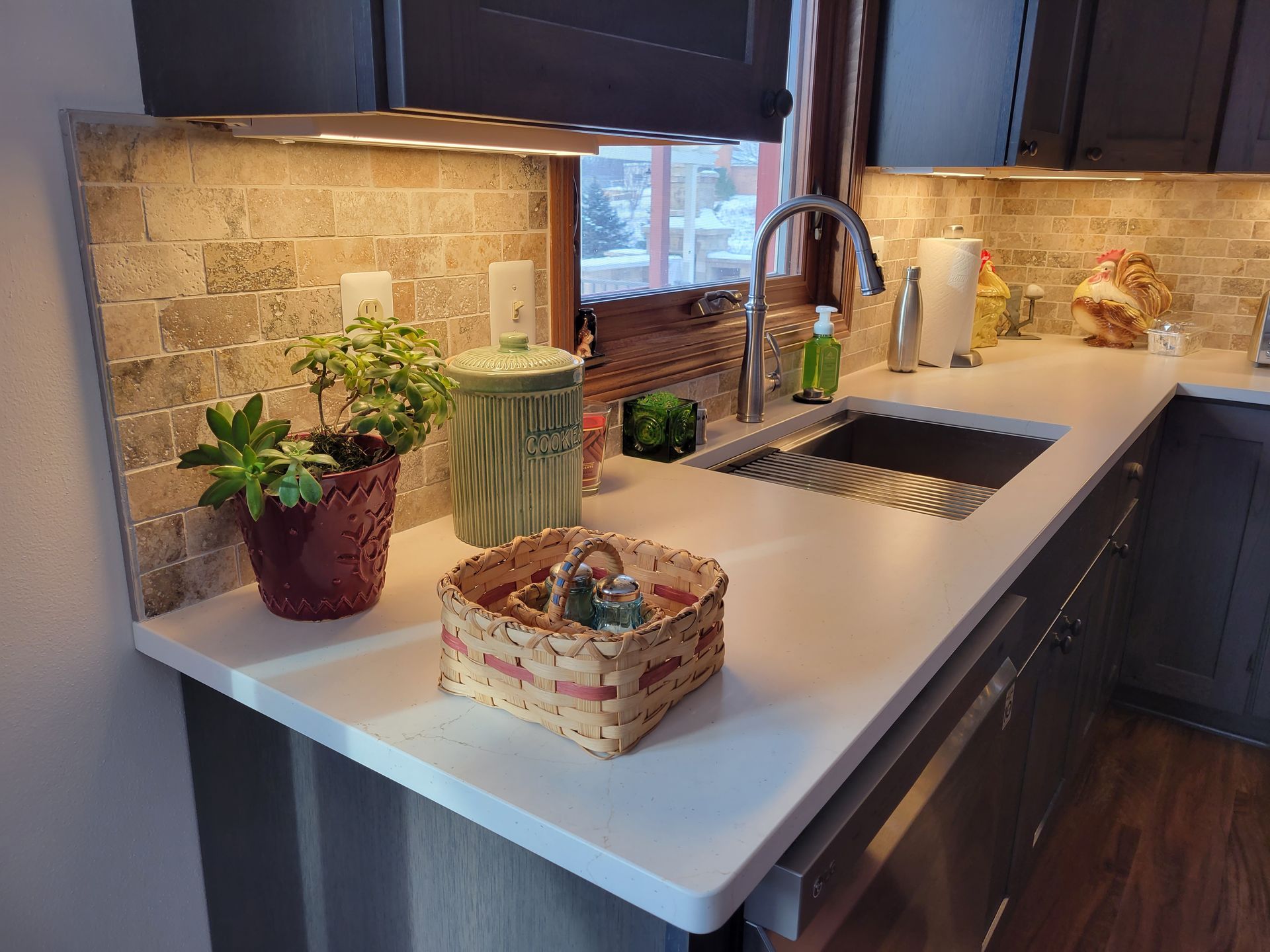 Modern kitchen countertop with sink, plants, and decorative baskets under warm under-cabinet lighting
