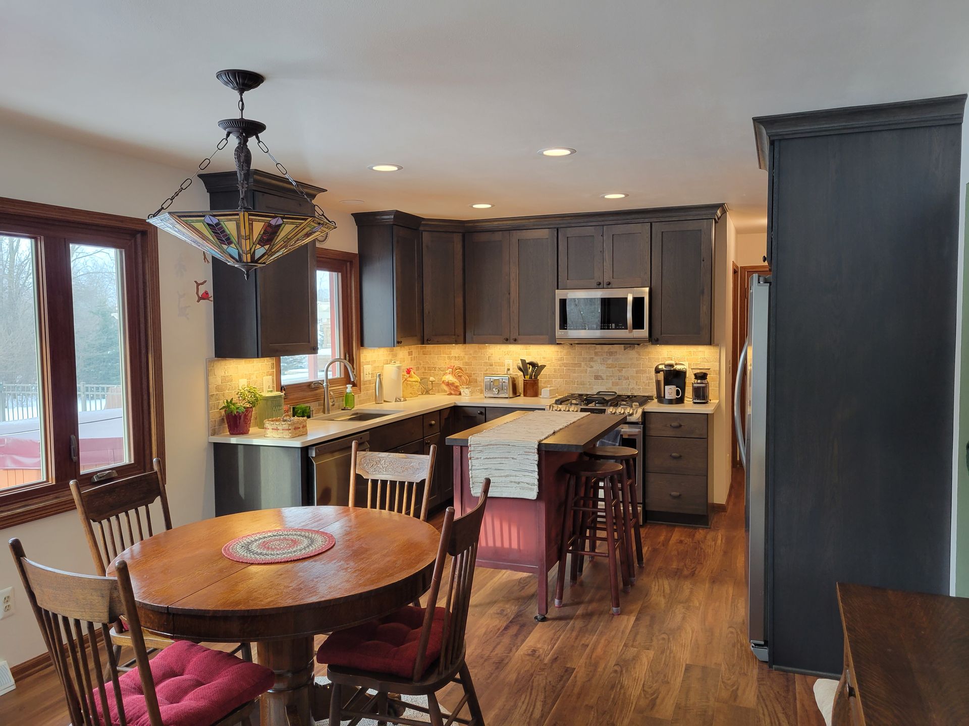 Dining area open to a modern kitchen with dark cabinets, wood table, stools, and pendant light.