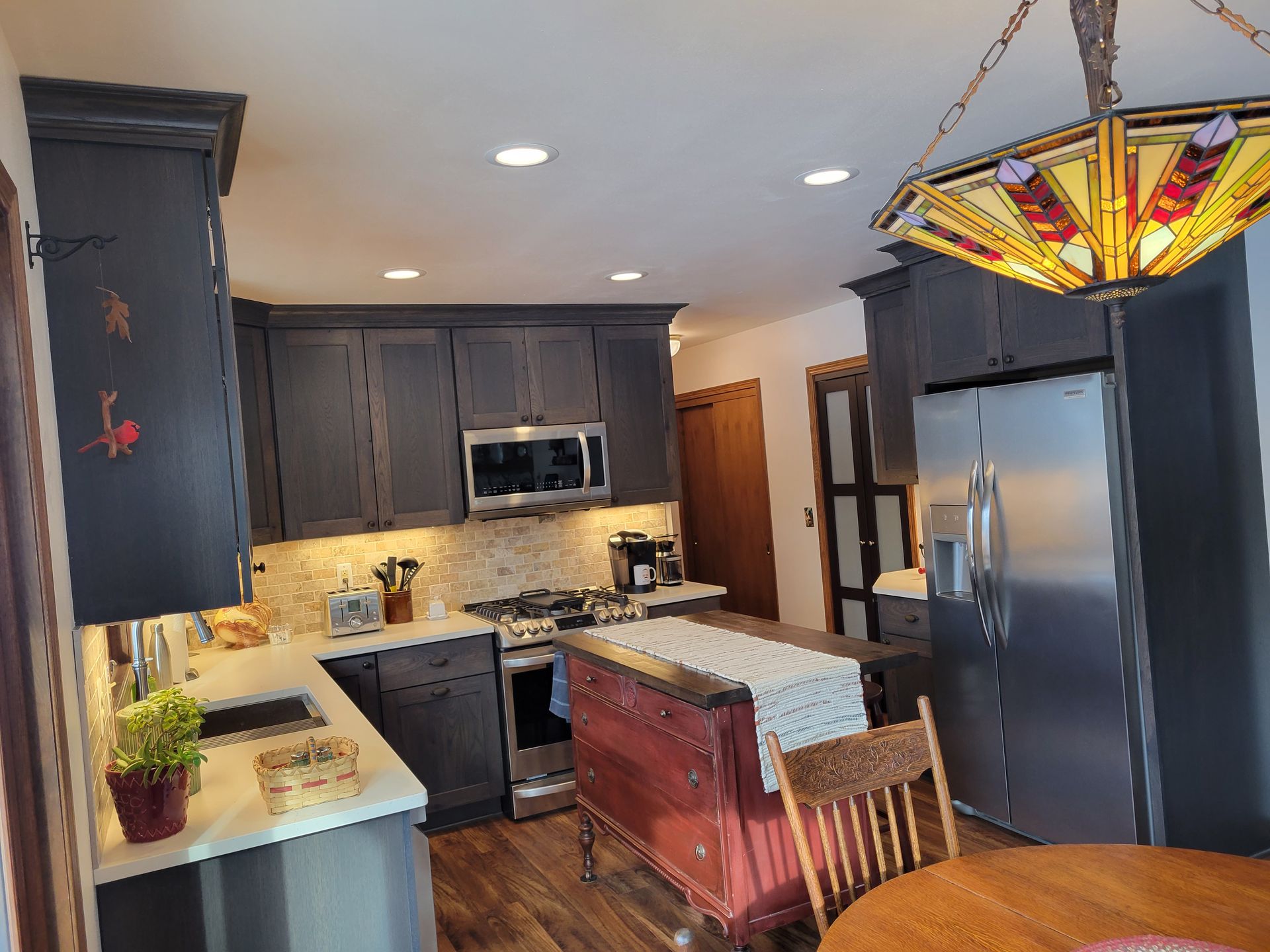 Modern kitchen with dark cabinets, granite counters, stainless appliances, and a dining table beneath a stained-glass light fixture