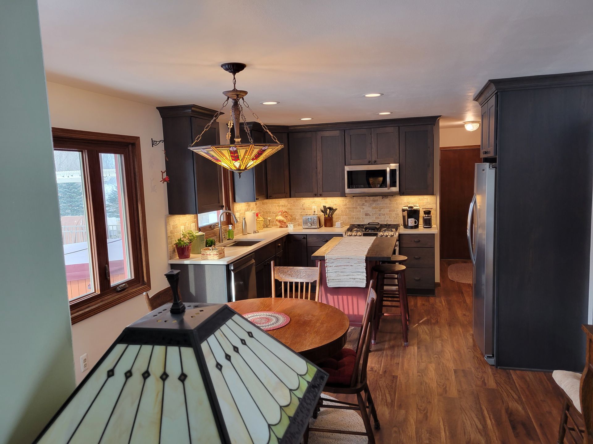 Modern kitchen with dark cabinets, wood floors, island seating, and a hanging stained-glass light.