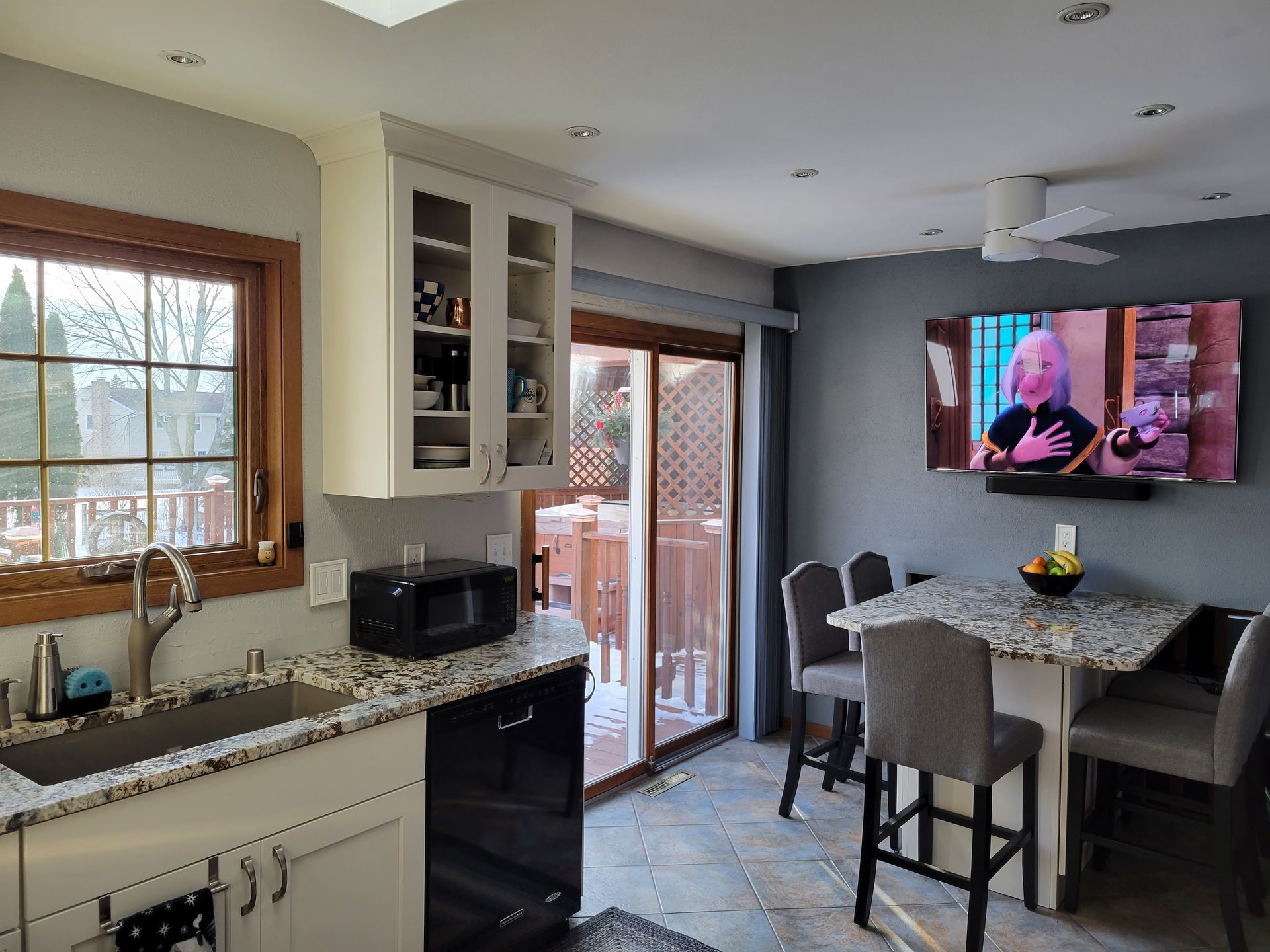 Bright kitchen and dining area with granite counters, sliding glass door, and TV mounted above the table.