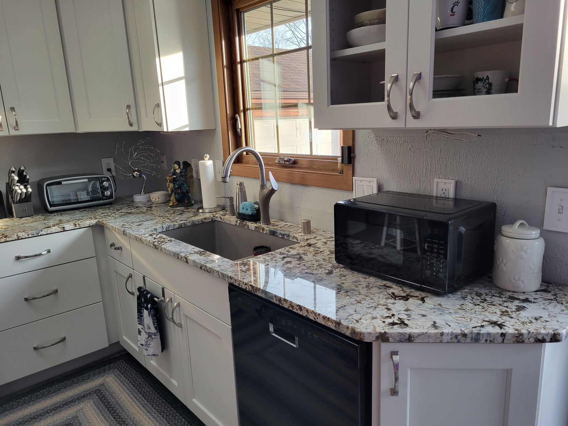 Bright kitchen counter with sink, toaster oven, cabinets, and speckled granite countertop.