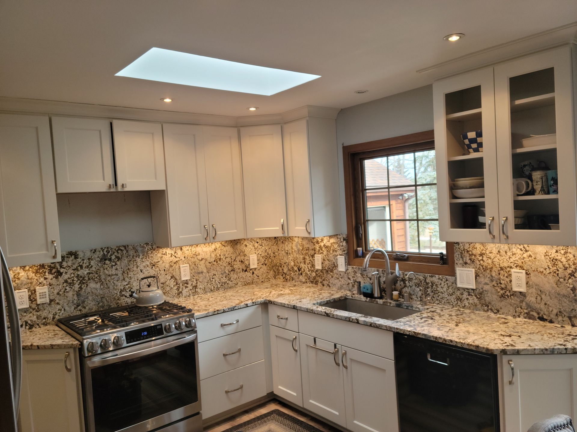 Modern kitchen with white cabinets, granite counters, stainless appliances, and a skylight.