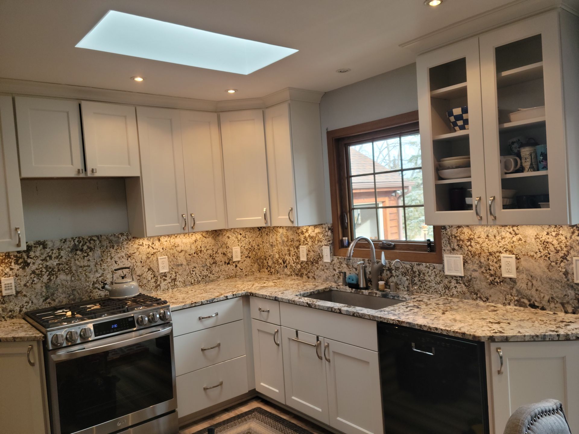 Bright kitchen with white cabinets, granite countertops, stainless appliances, and a skylight above the sink.