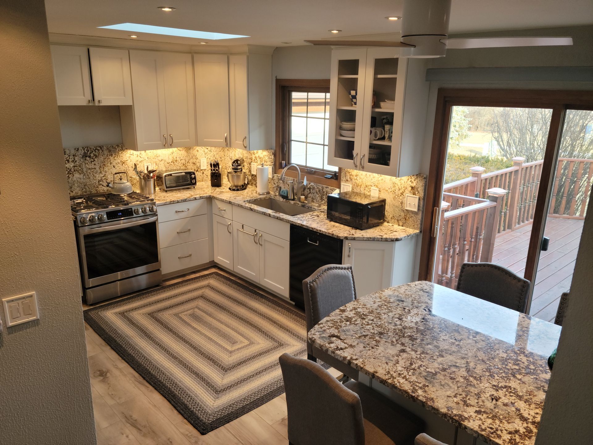 Bright kitchen with white cabinets, granite counters, striped rug, and sliding glass door to a deck