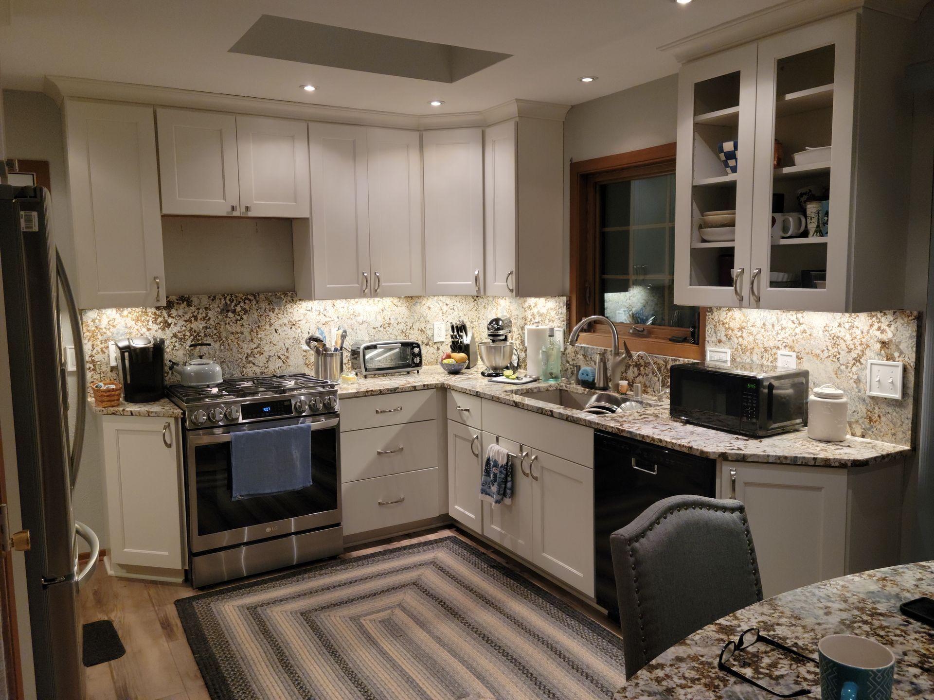 Modern kitchen with white cabinets, granite counters, and a patterned rug, lit by under-cabinet lights