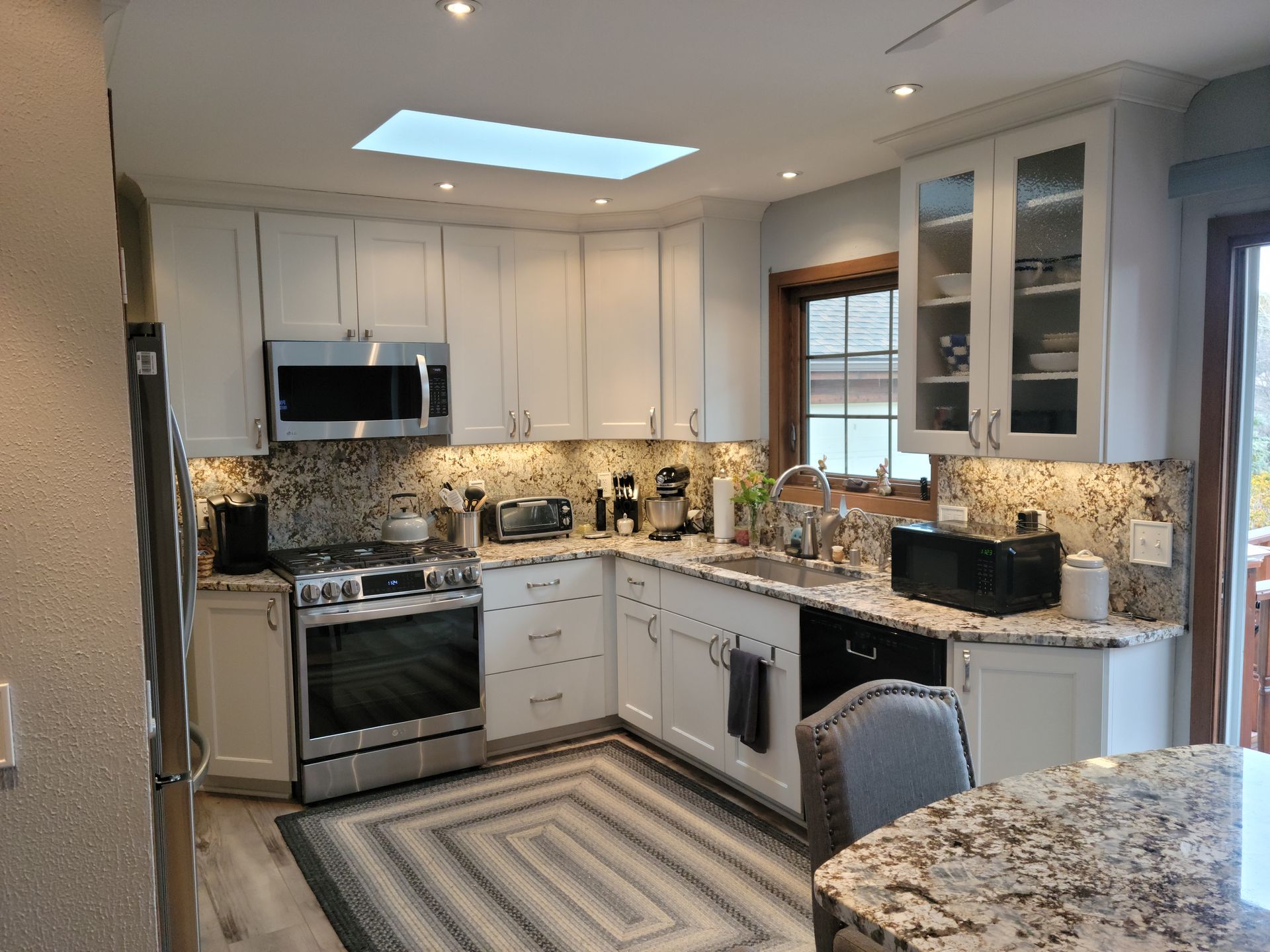 Bright modern kitchen with white cabinets, granite counters, stainless appliances, and a striped rug.