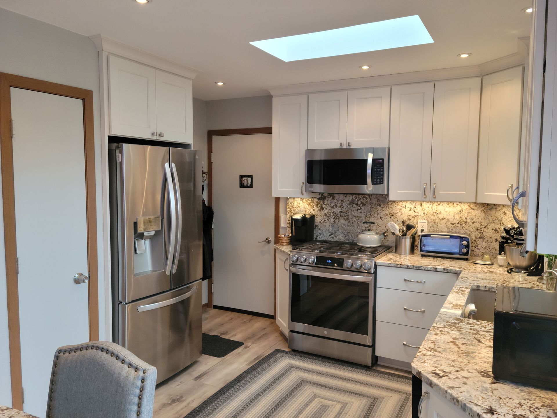 Modern kitchen with stainless steel appliances, white cabinets, granite counters, and a skylight