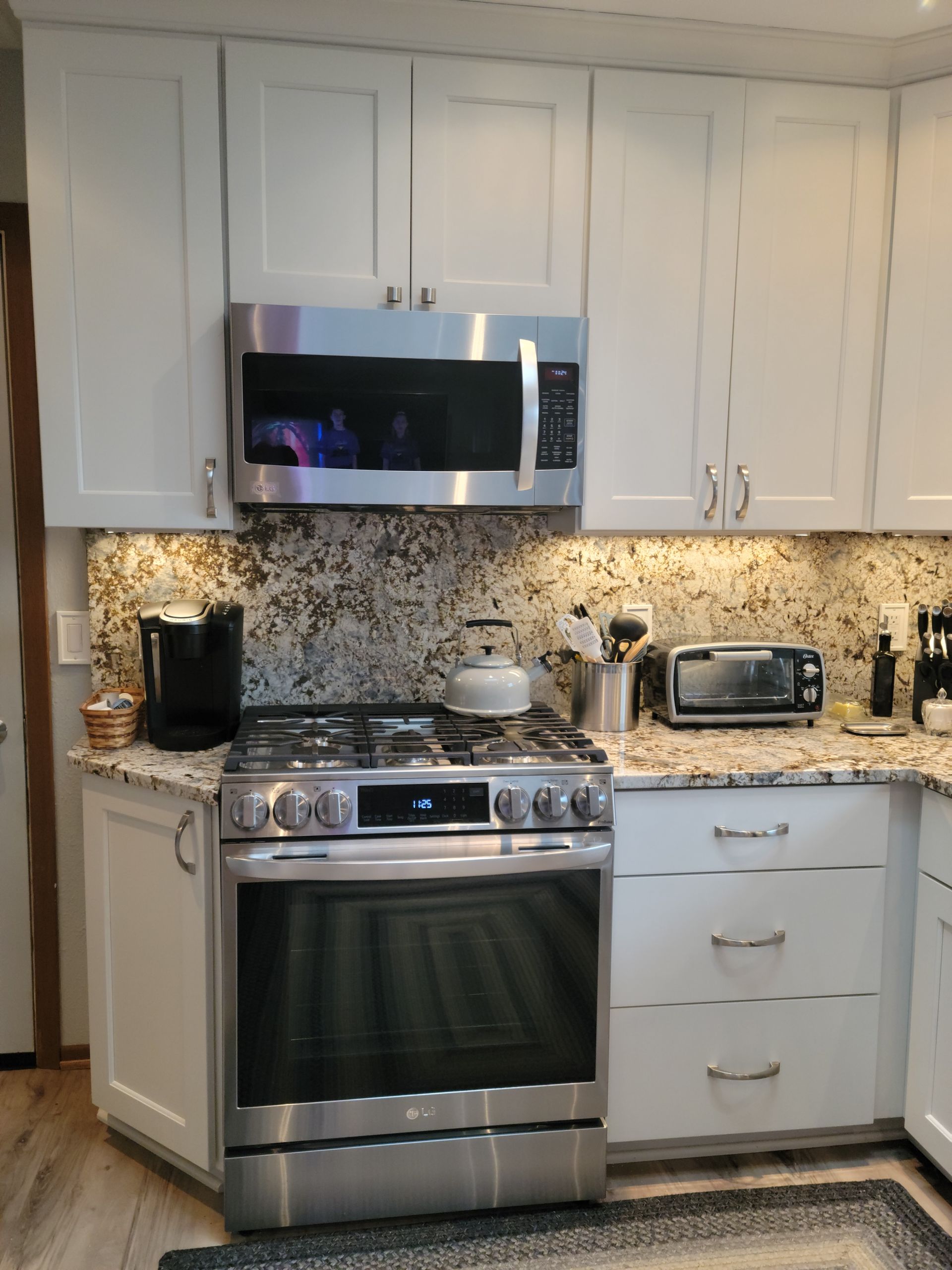 Modern kitchen with white cabinets, stainless steel stove and microwave, speckled backsplash, and small countertop appliances