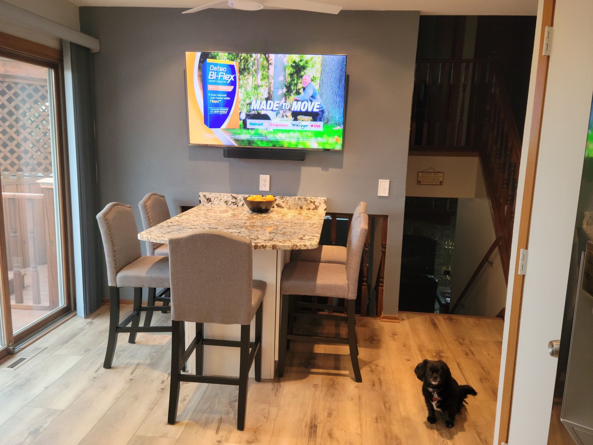Dining area with wall-mounted TV, table set for a meal, and a black dog on the hardwood floor