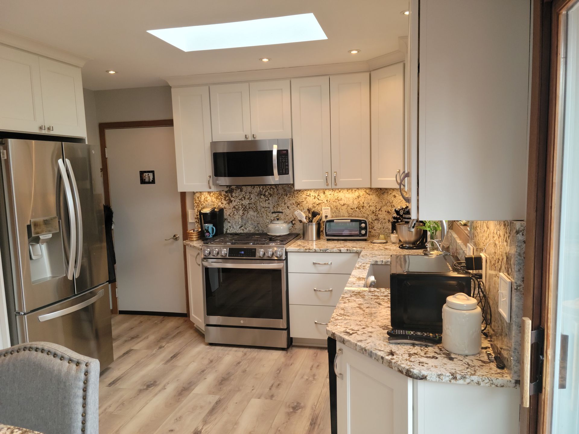 Bright modern kitchen with white cabinets, stainless appliances, granite counters, and light wood flooring