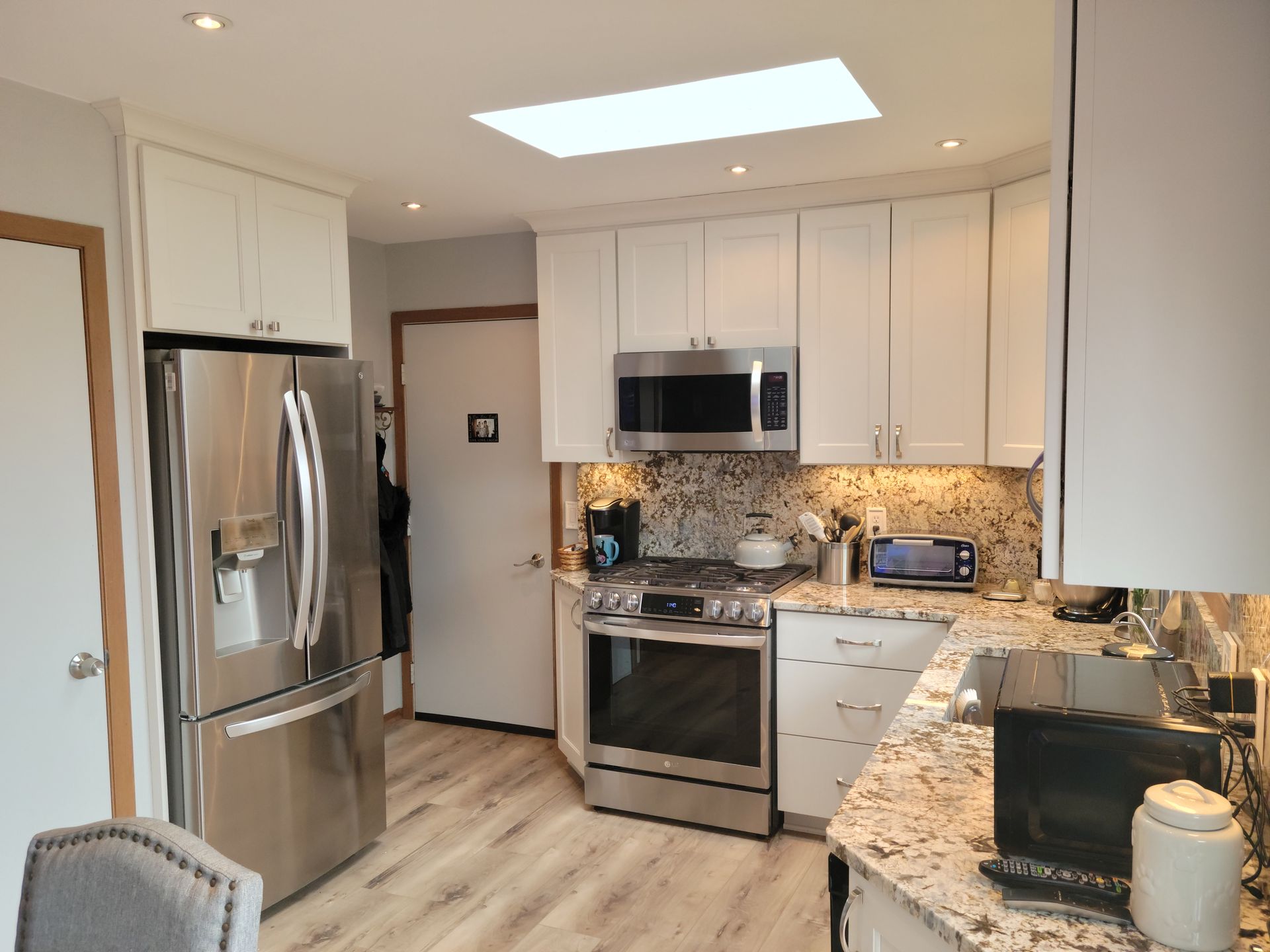 Modern kitchen with stainless steel appliances, white cabinets, granite counters, and a skylight