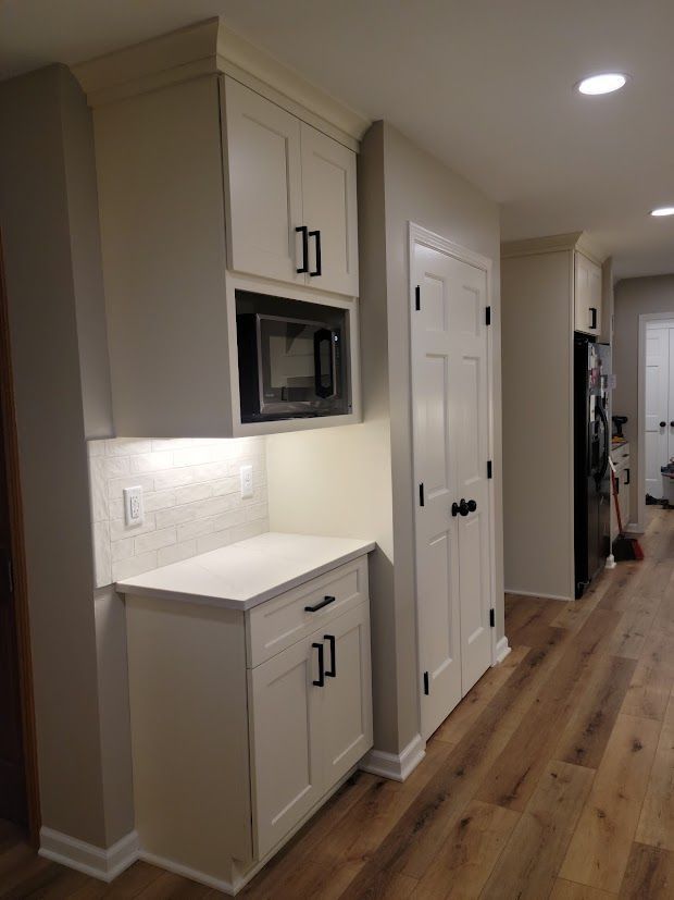Narrow hallway with beige cabinets, built-in microwave, white doors, and wood flooring.
