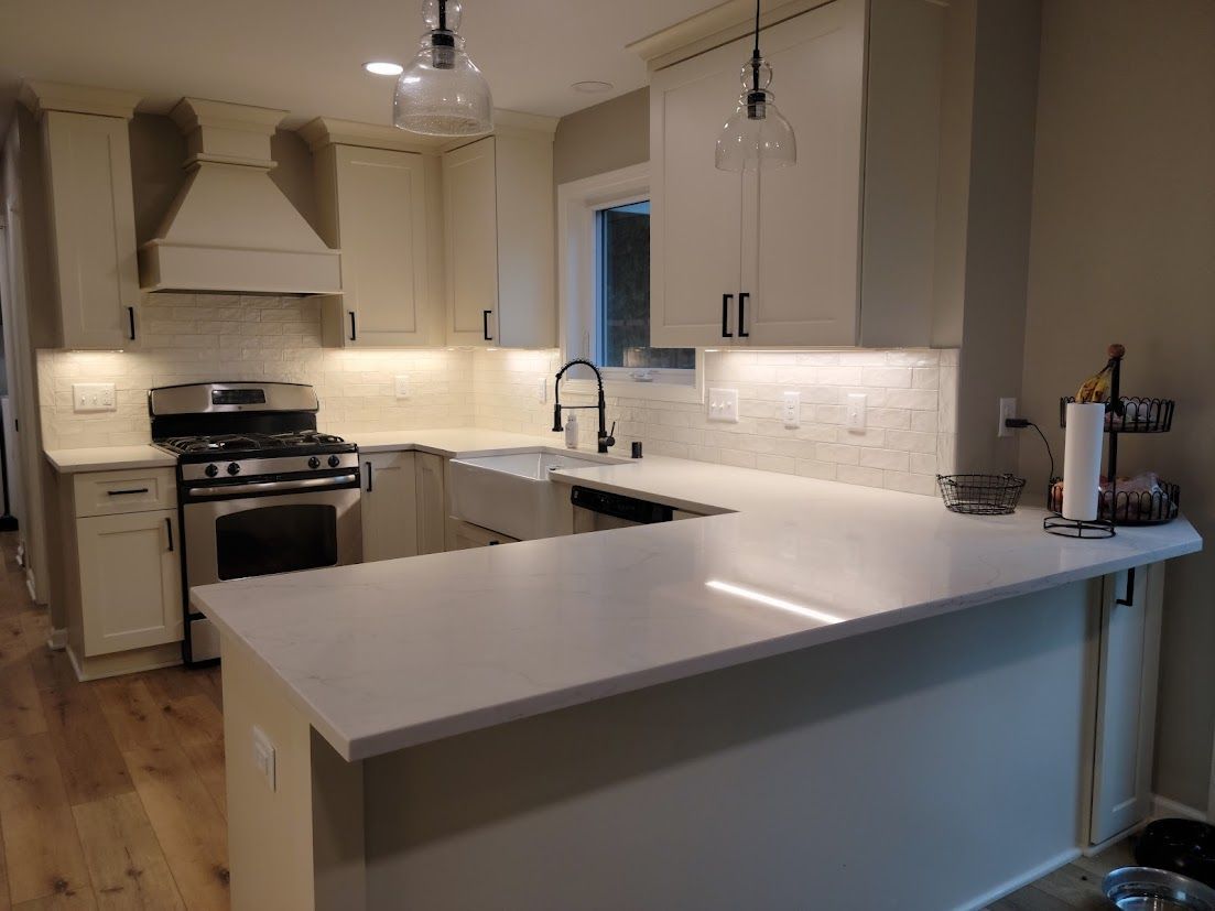 Bright modern kitchen with white cabinets, island, stainless stove, and pendant lights.