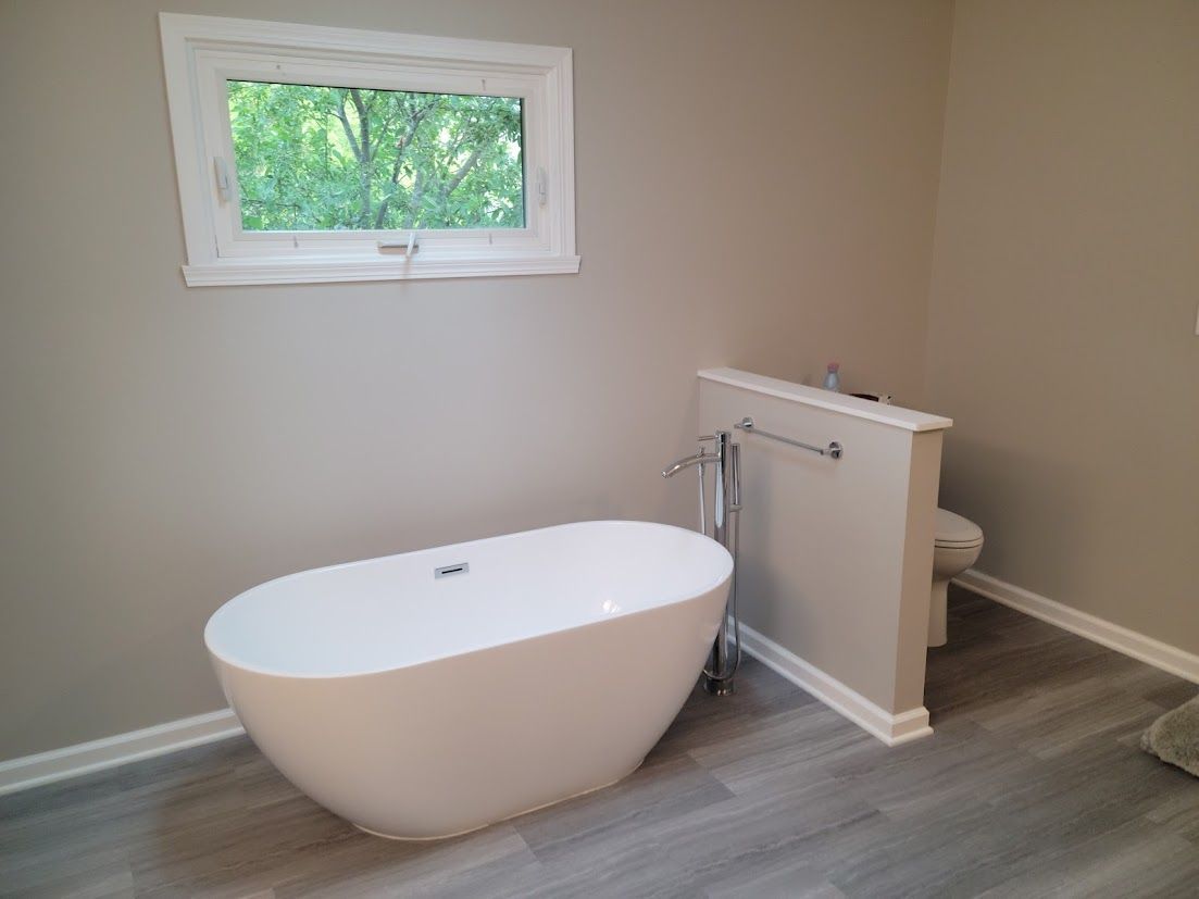 Modern bathroom with freestanding tub, window, and wood-look flooring