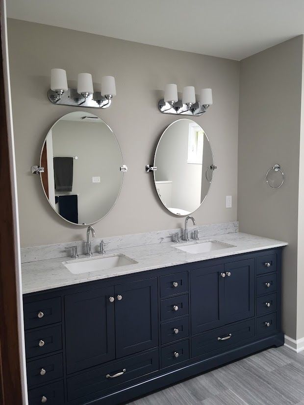 Modern bathroom vanity with two round mirrors, white countertop, and navy cabinets