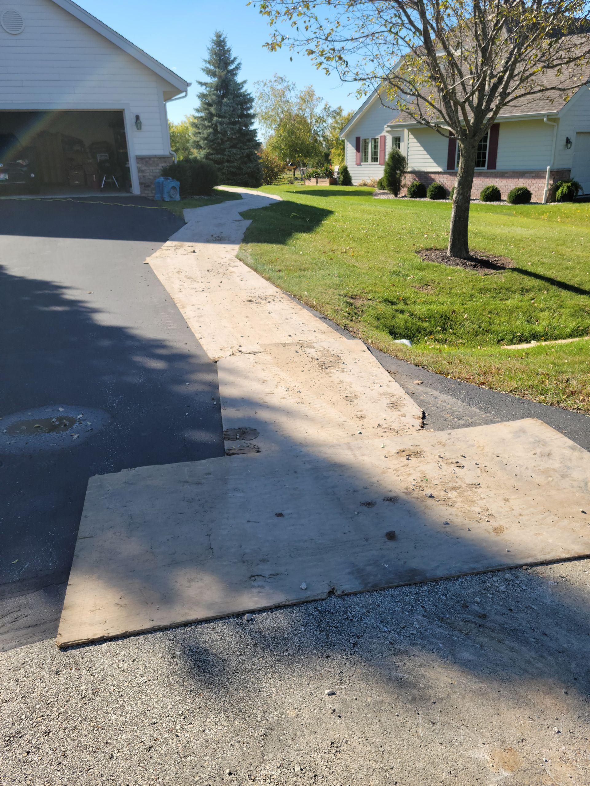 Damaged asphalt driveway with a large patch of exposed sand near a suburban house