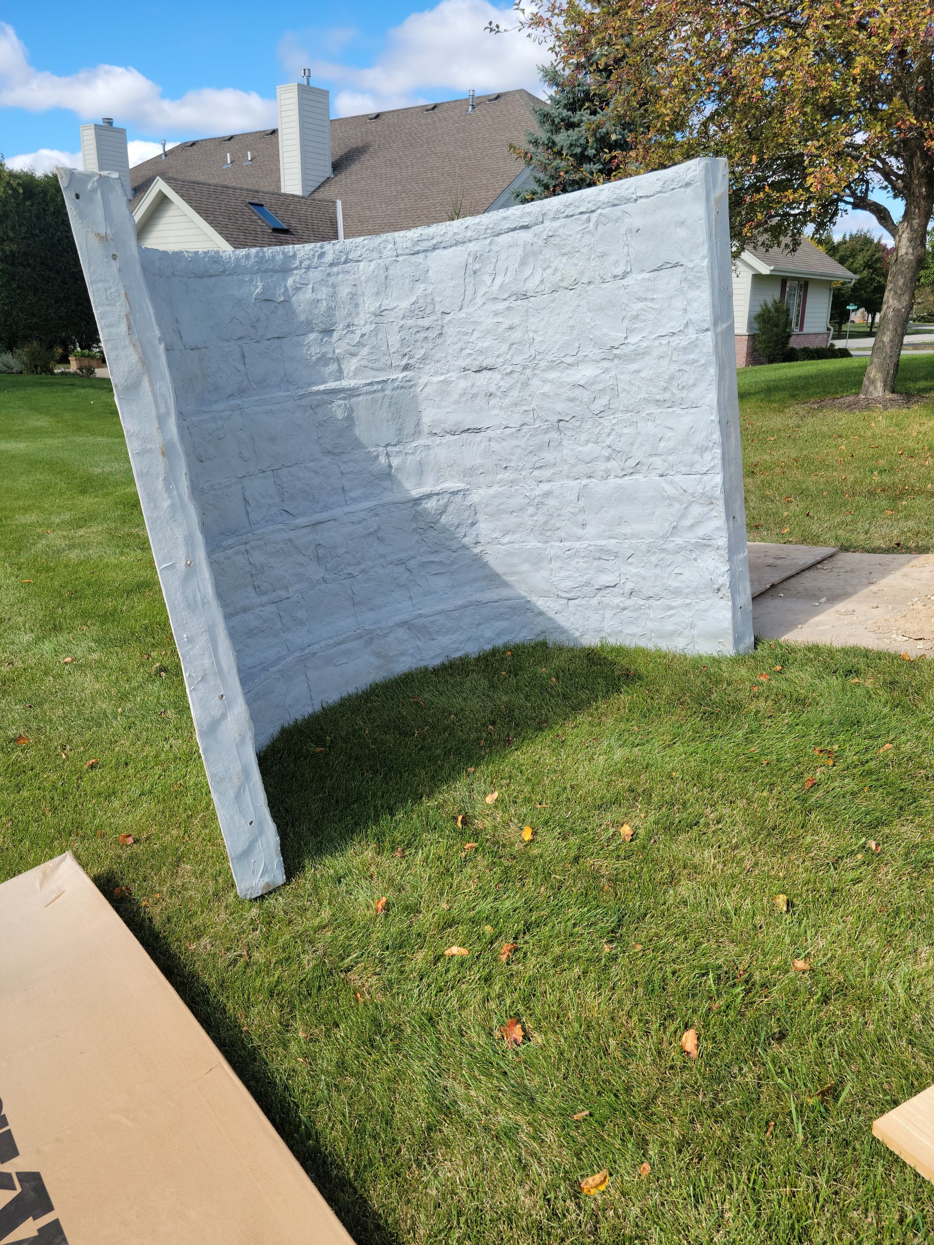 White curved outdoor privacy screen on a lawn beside a sidewalk and houses.