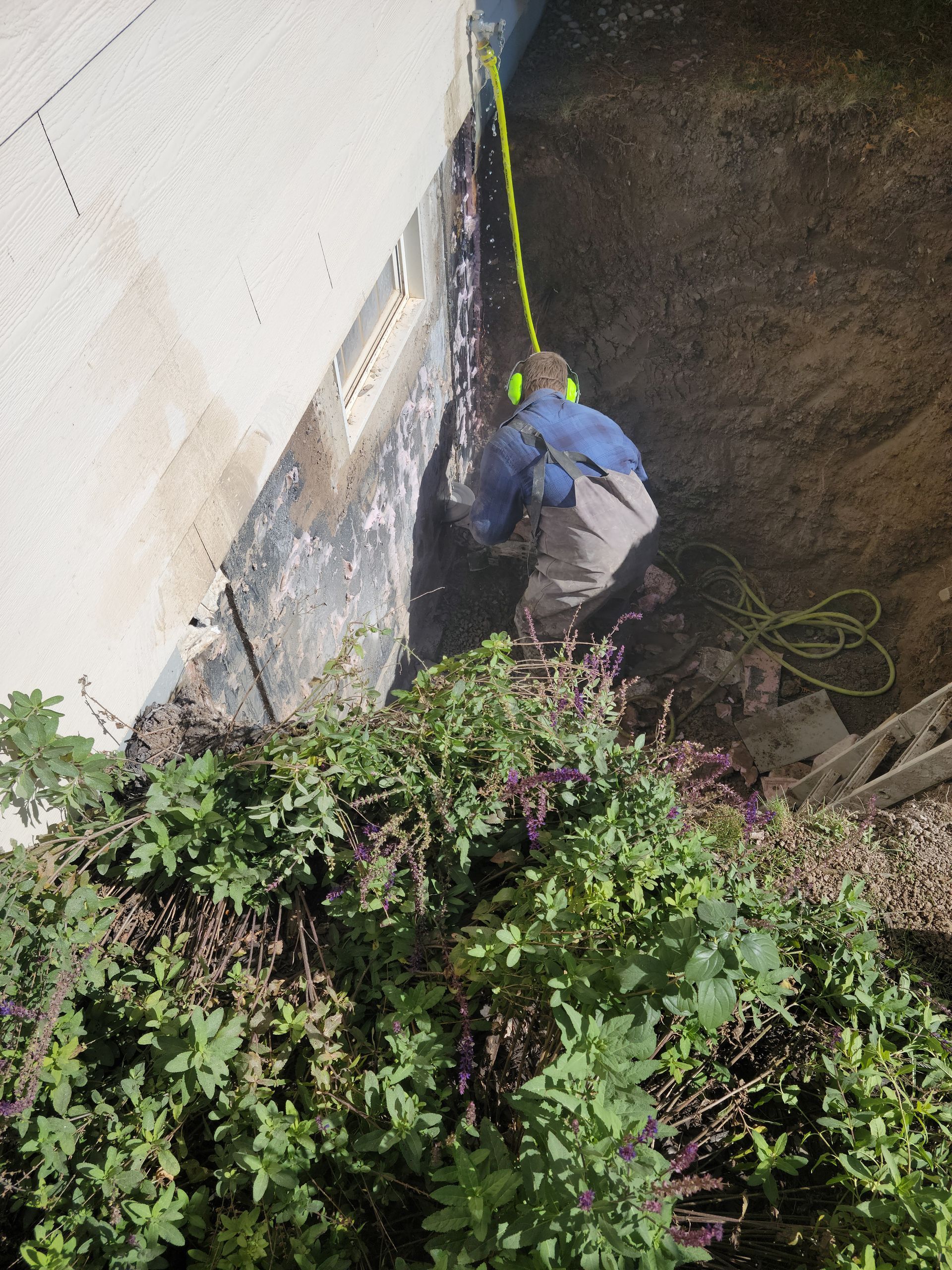 Worker in blue jacket climbing a rope beside a wall in a steep dirt area with dense plants below