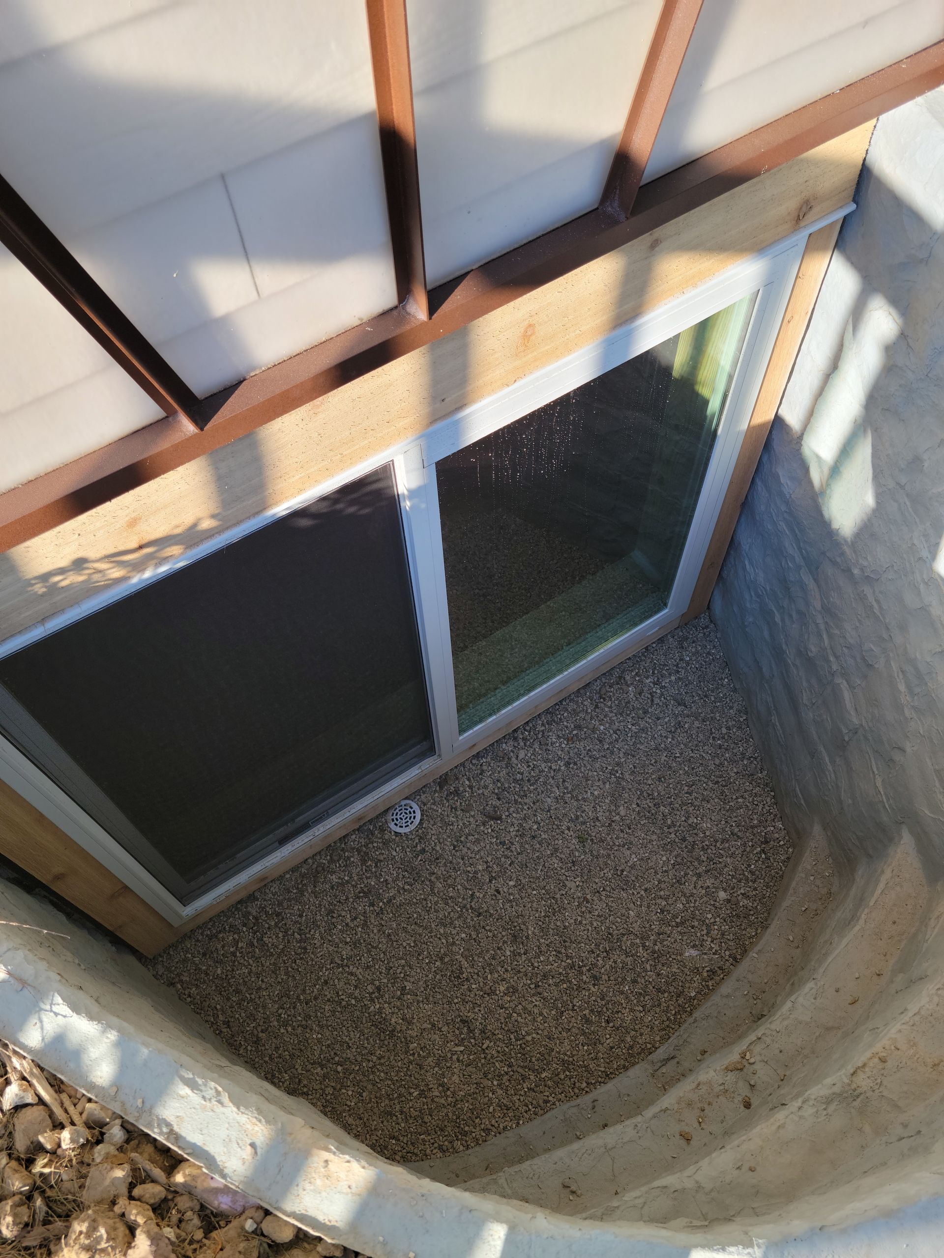 Looking down into a gravel-lined courtyard beside a building with windows and curved concrete walls.