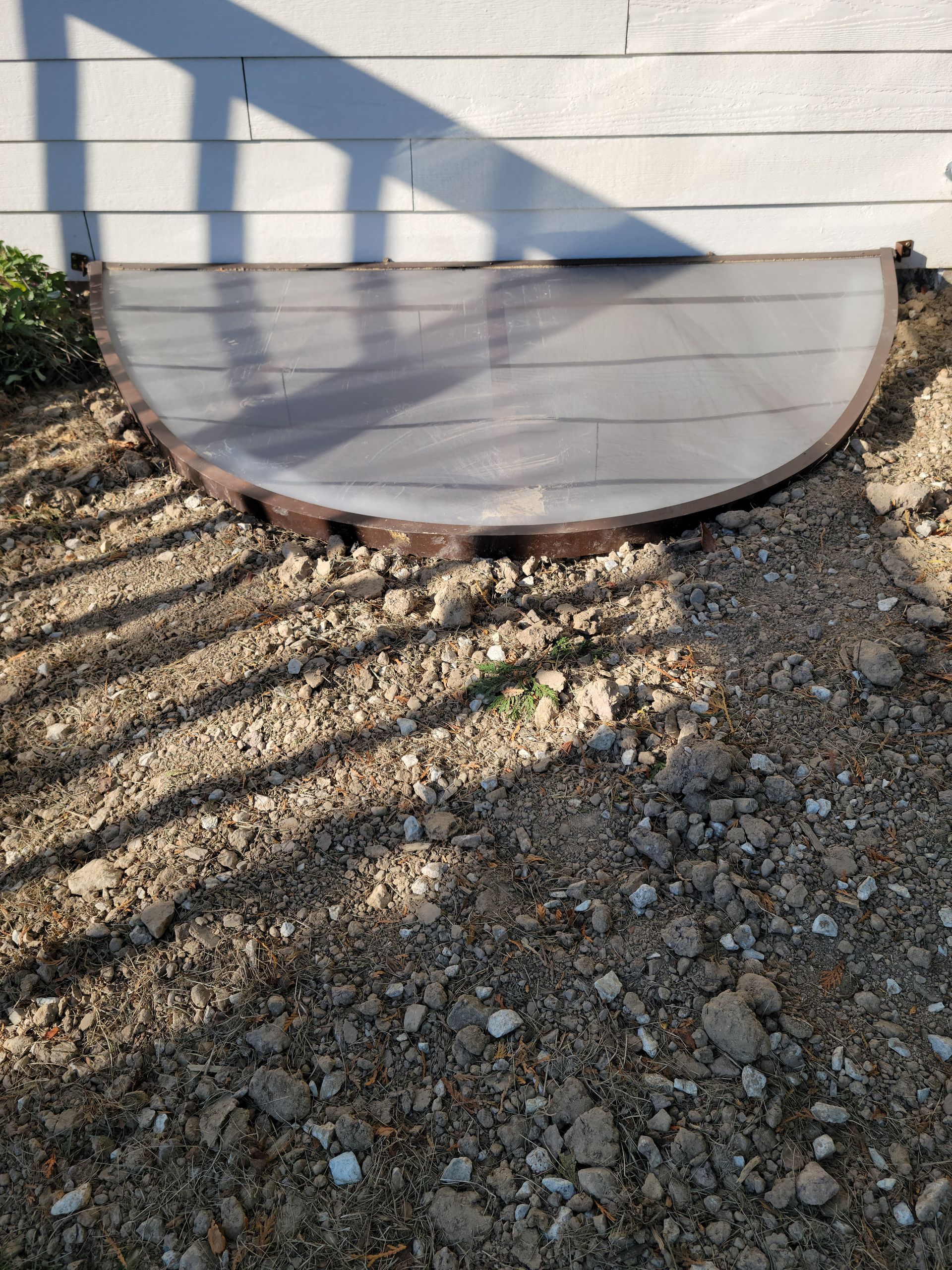 Half-buried white half-circle vent cover against a beige wall on gravel ground