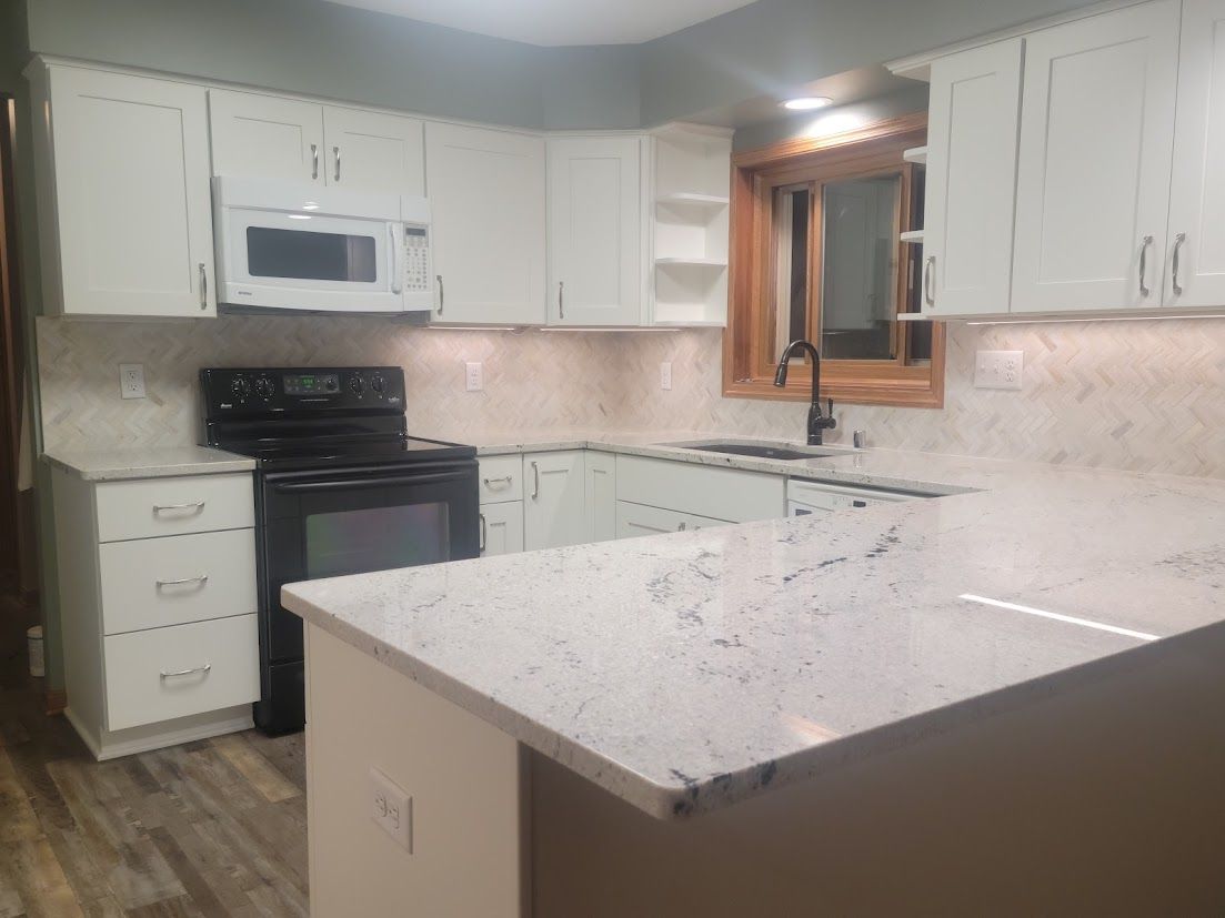 Bright white kitchen with marble island, white cabinets, black stove, and small window above the sink