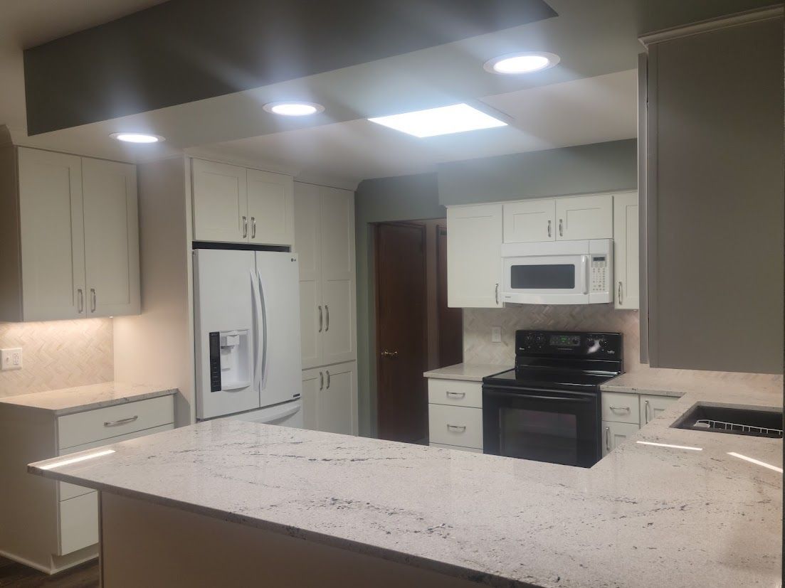 Modern kitchen with white cabinets, granite island, stainless fridge, stove, and recessed ceiling lights