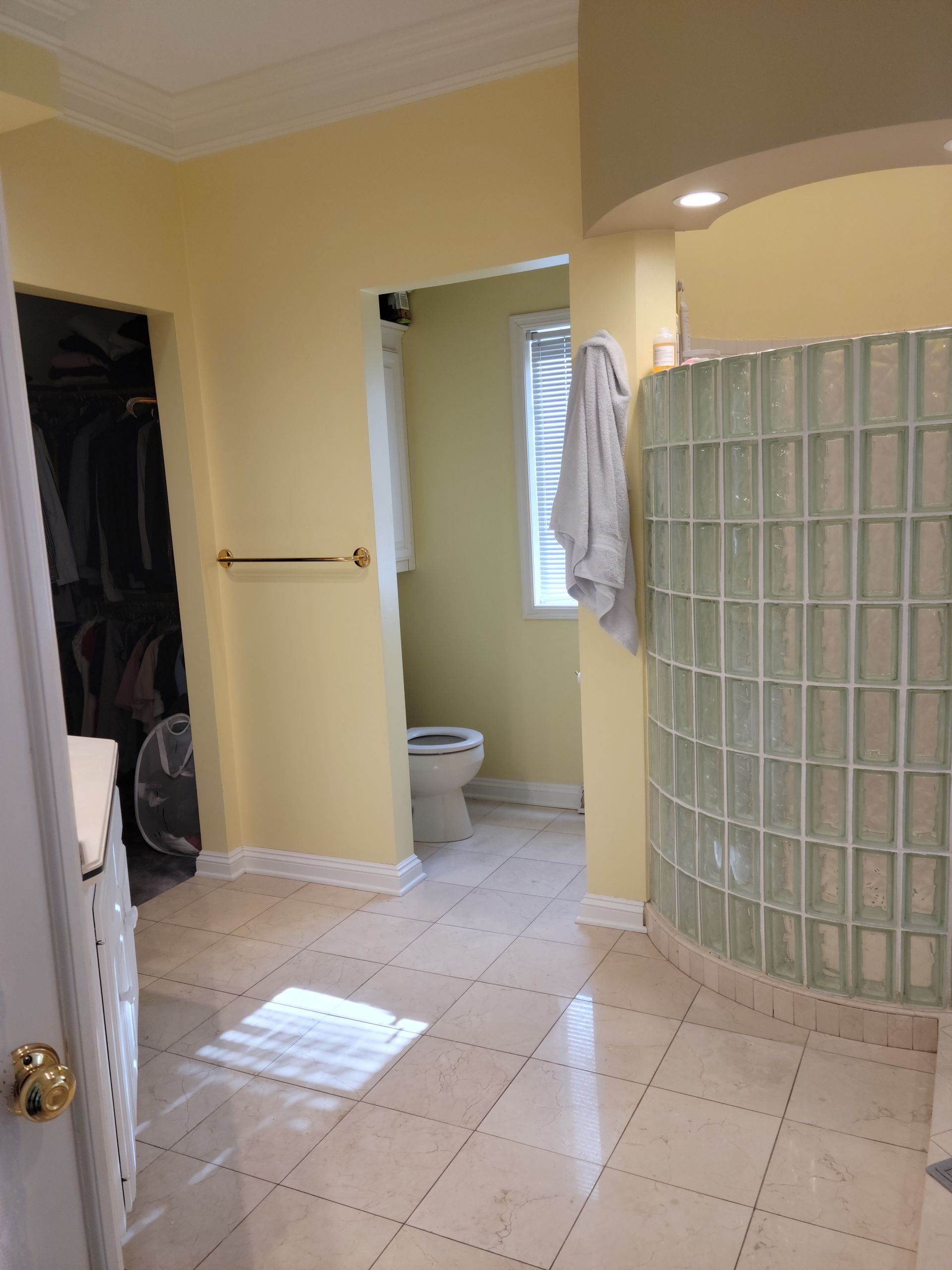 Bathroom interior with pale yellow walls, tiled floor, glass-block shower, and open doorway to toilet area