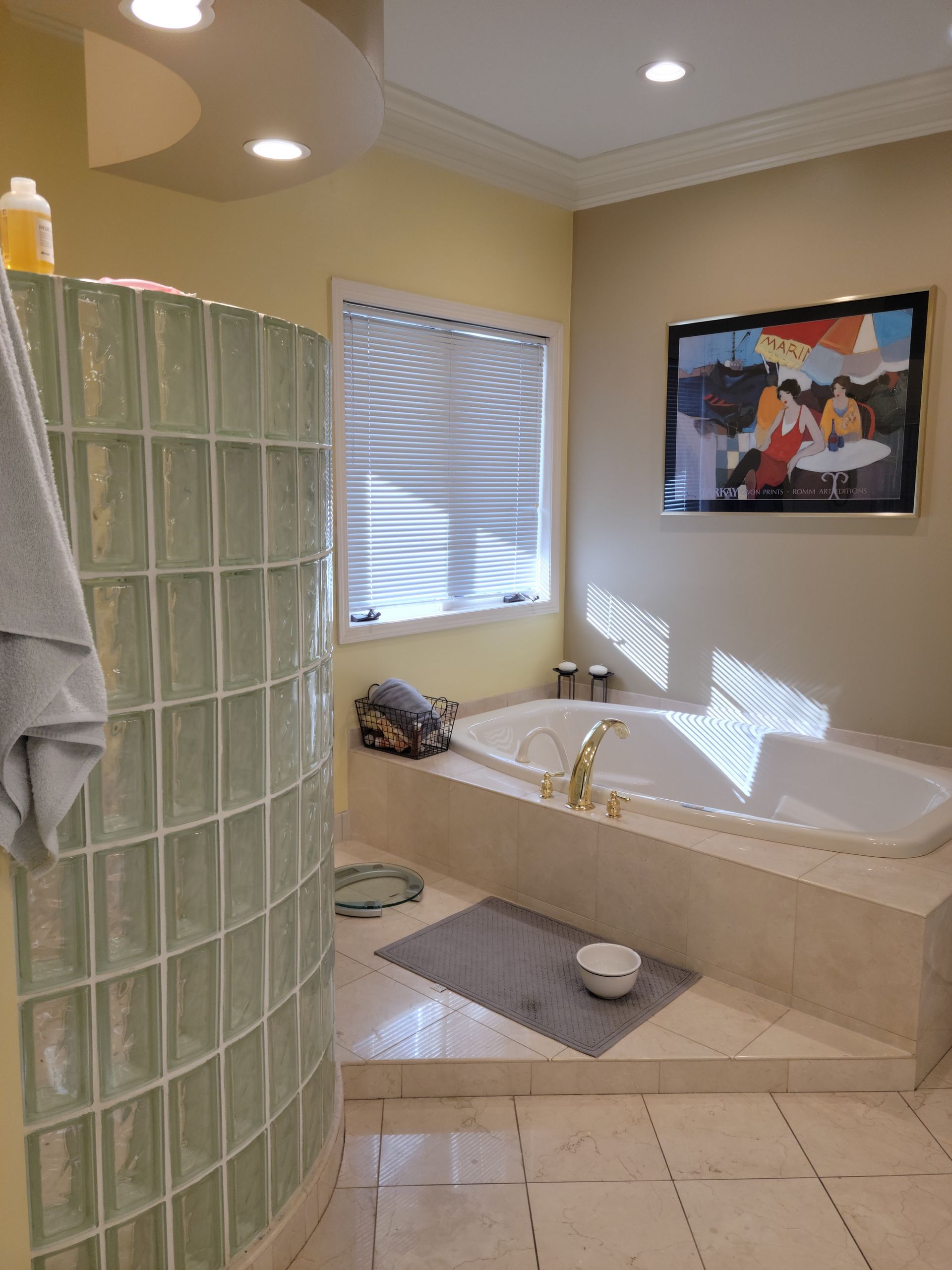 Bathroom with glass block shower, corner tub, beige tile, and sunlight through blinds.