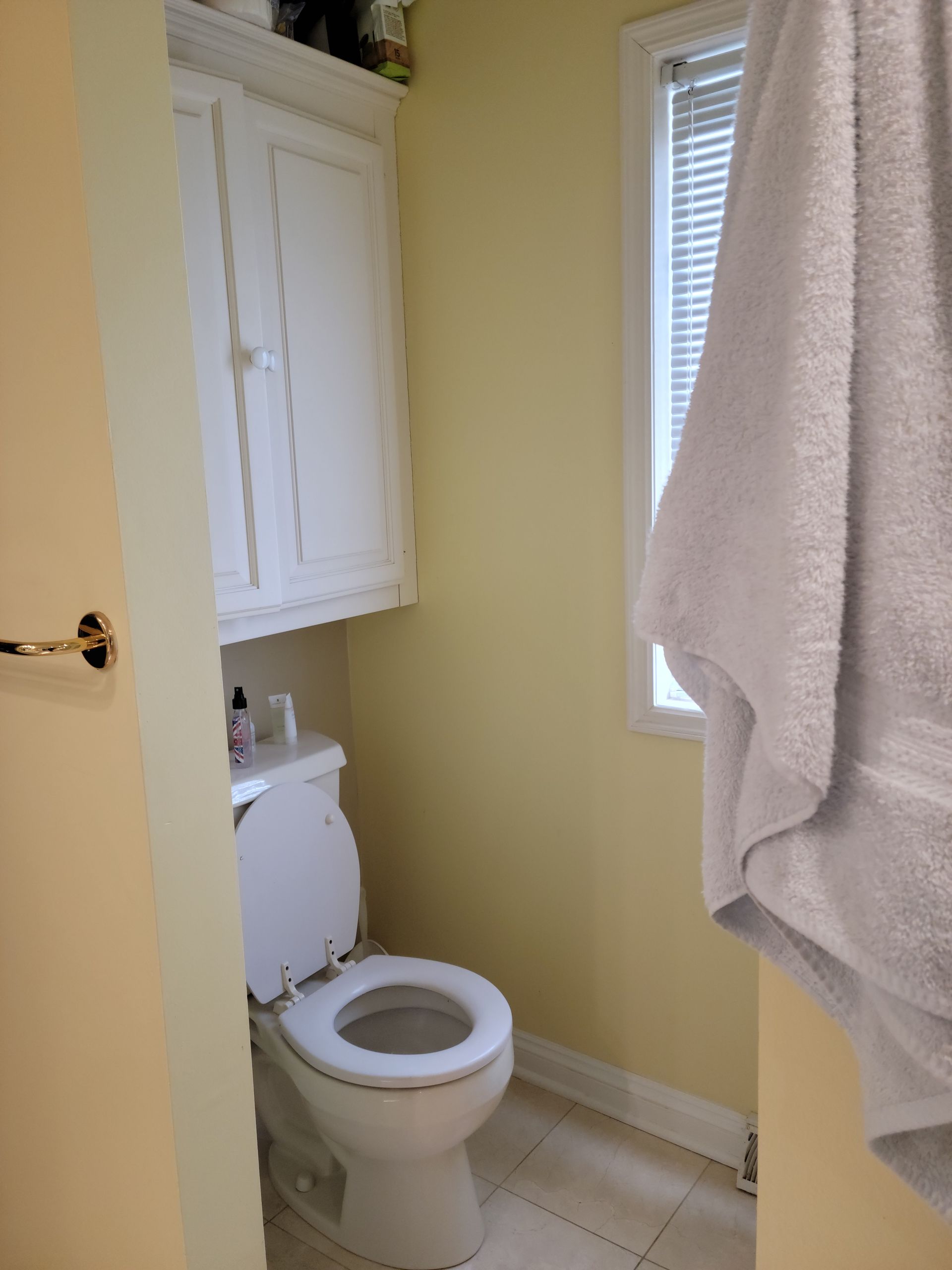 Small bathroom with a toilet, white cabinet, yellow walls, and a towel hanging by the window.
